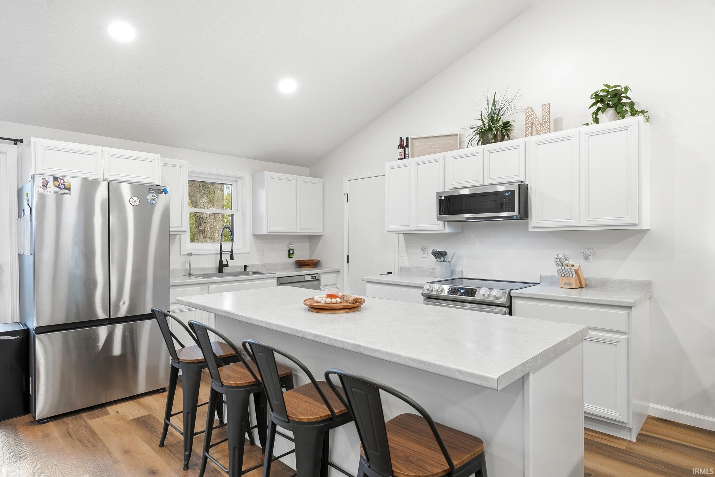 Kitchen featuring a center island, white cabinetry, stainless steel appliances, and wood-finish flooring