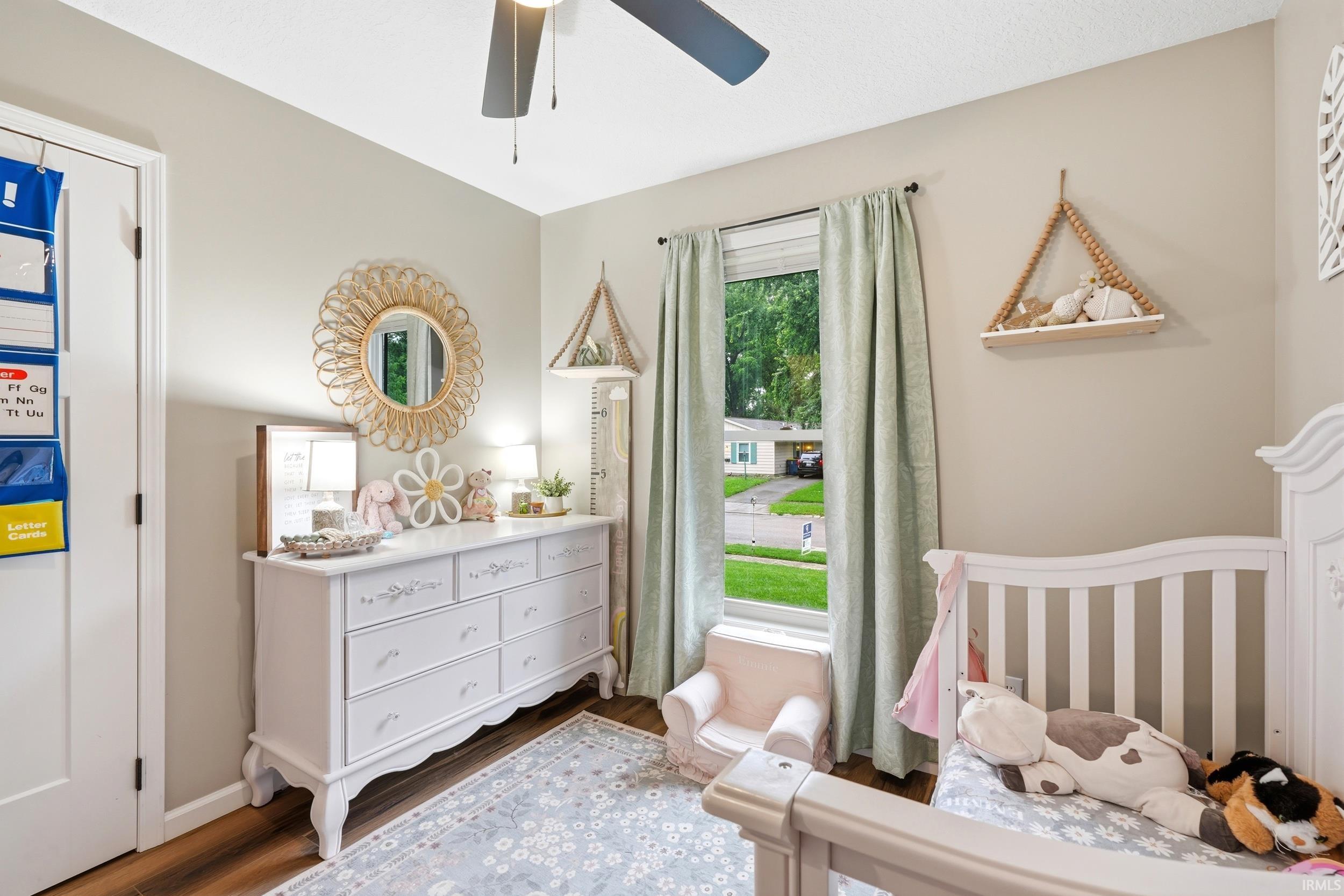 Warm-toned walls complement wood-finish flooring in this space featuring a ceiling fan, a window with natural light, and a built-in wall shelf