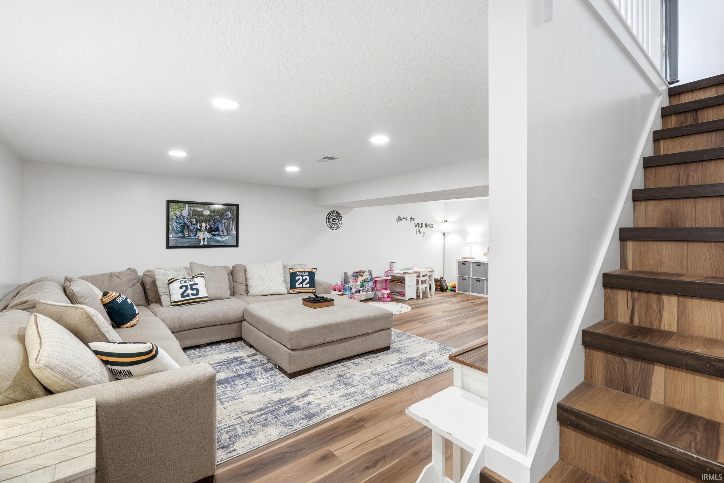 Finished lower level featuring recessed lighting, wood-finish flooring, a painted white staircase with wood treads, and white interior walls
