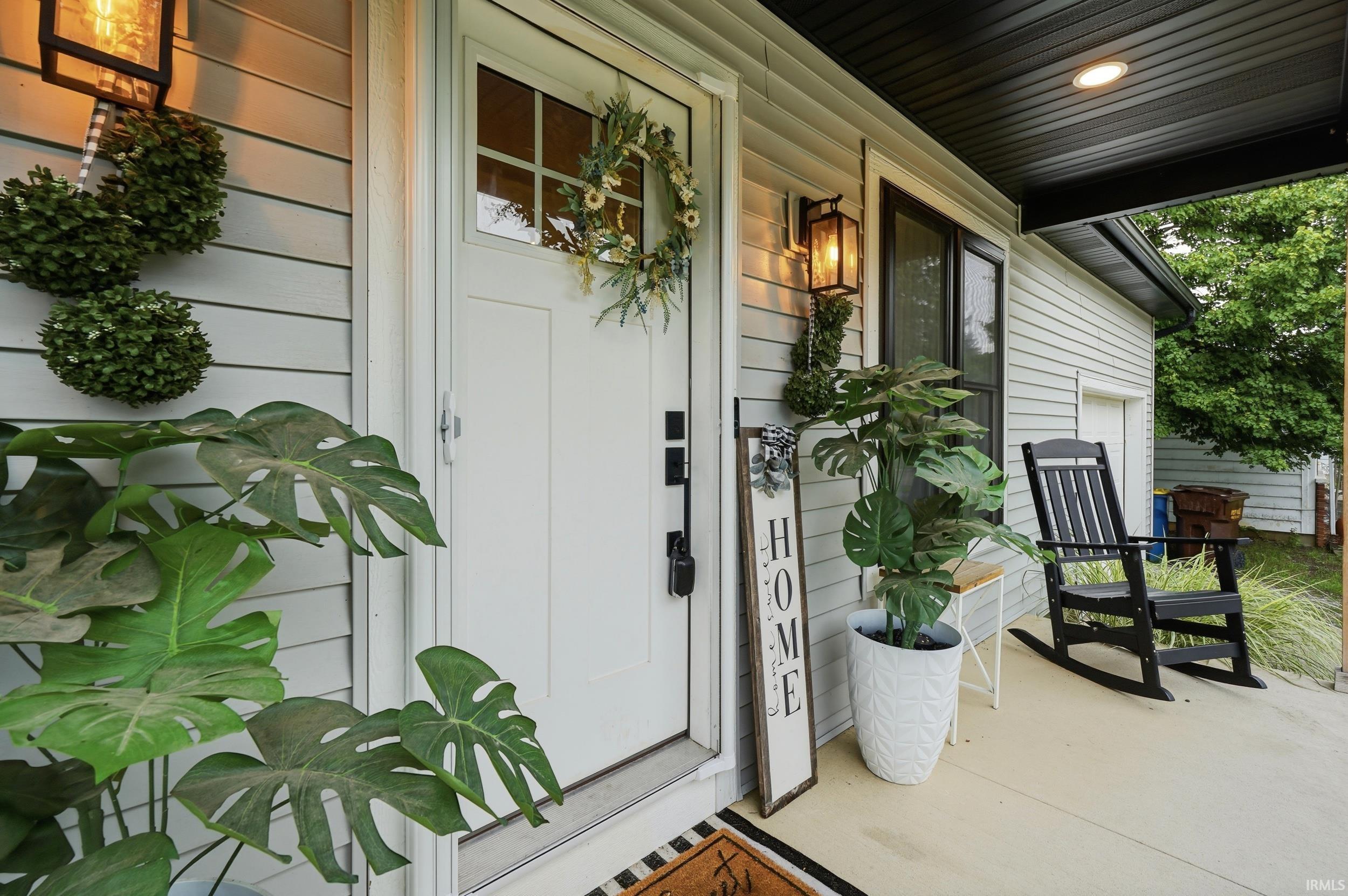Front entrance featuring a white door with transom window, light gray siding, covered porch, and exterior lantern lighting