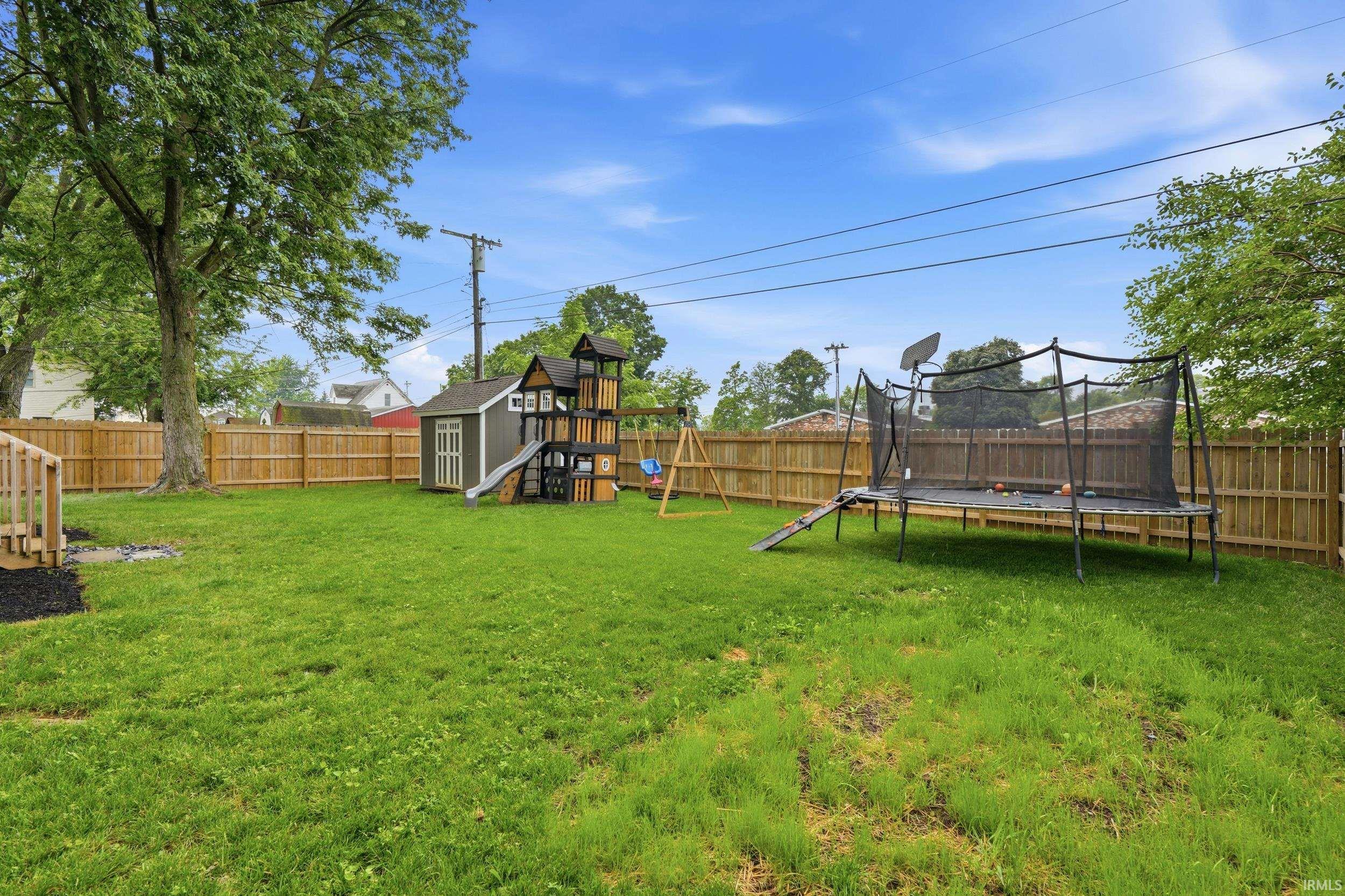Expansive backyard featuring a lush green lawn, full wood privacy fencing, and mature trees