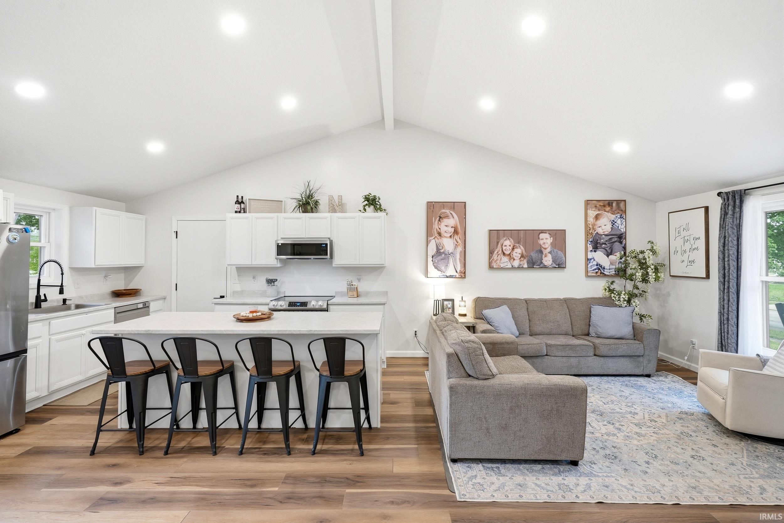 Open-concept living space featuring a vaulted ceiling with recessed lighting, wood-finish flooring, and a kitchen island with seating