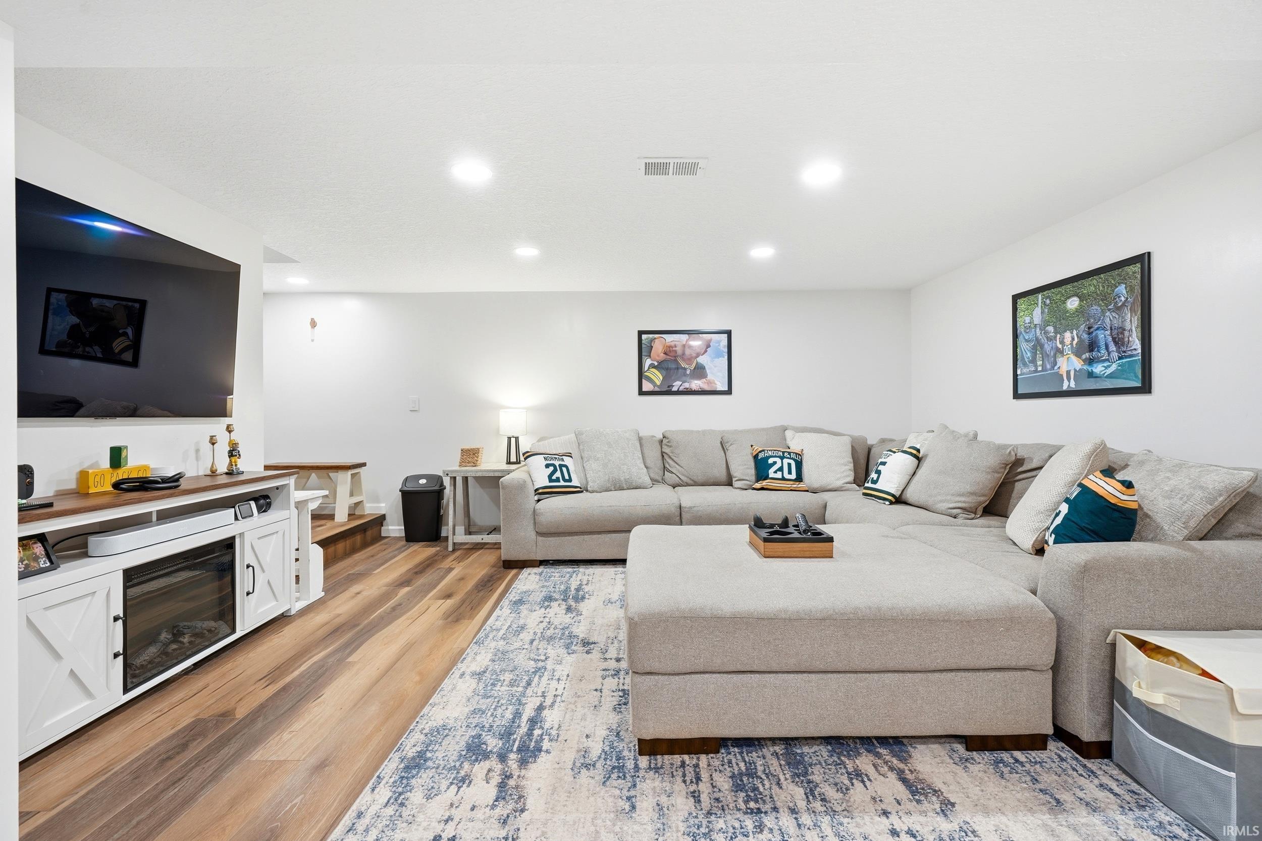 Spacious living area featuring wood-finish flooring, recessed lighting, and a built-in media console with an electric fireplace