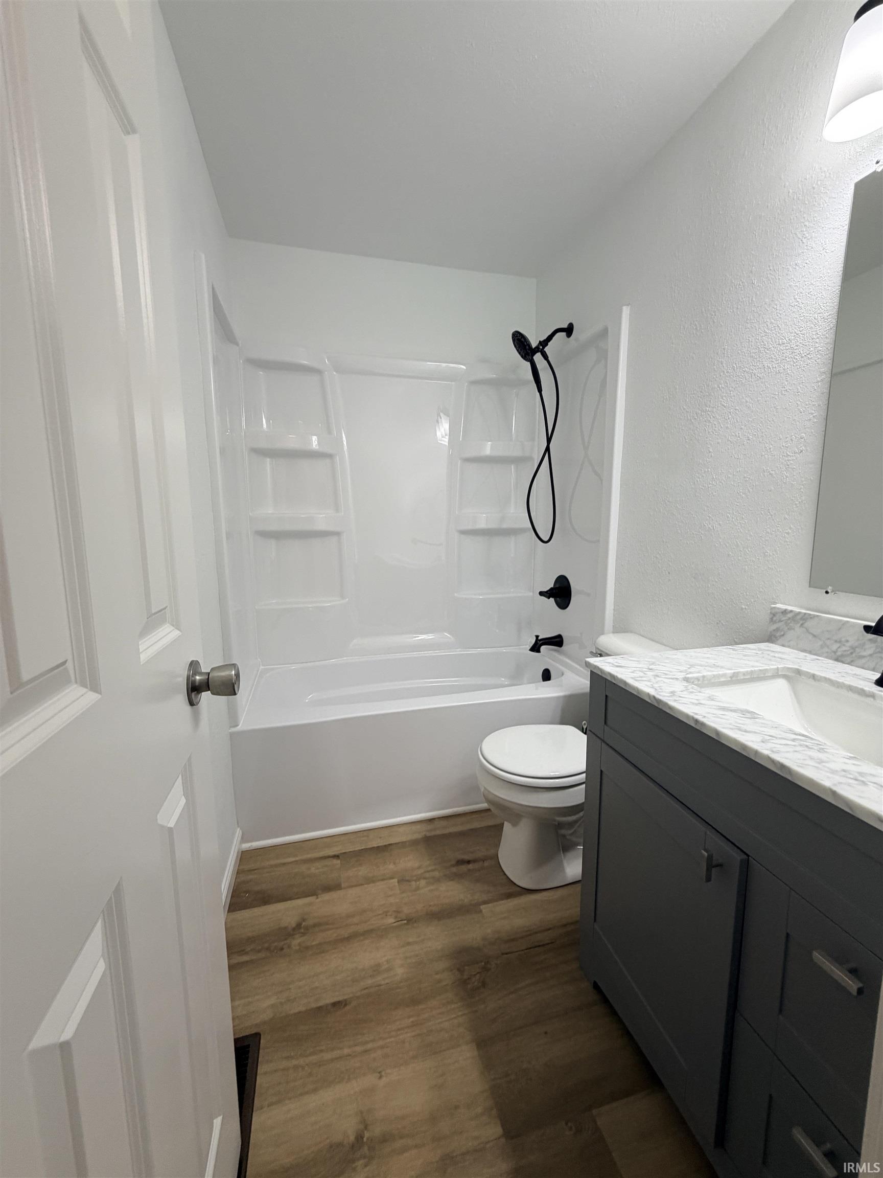 Bathroom featuring a white tub/shower combination with black fixtures, wood-finish flooring, and a vanity with a white countertop and undermount sink