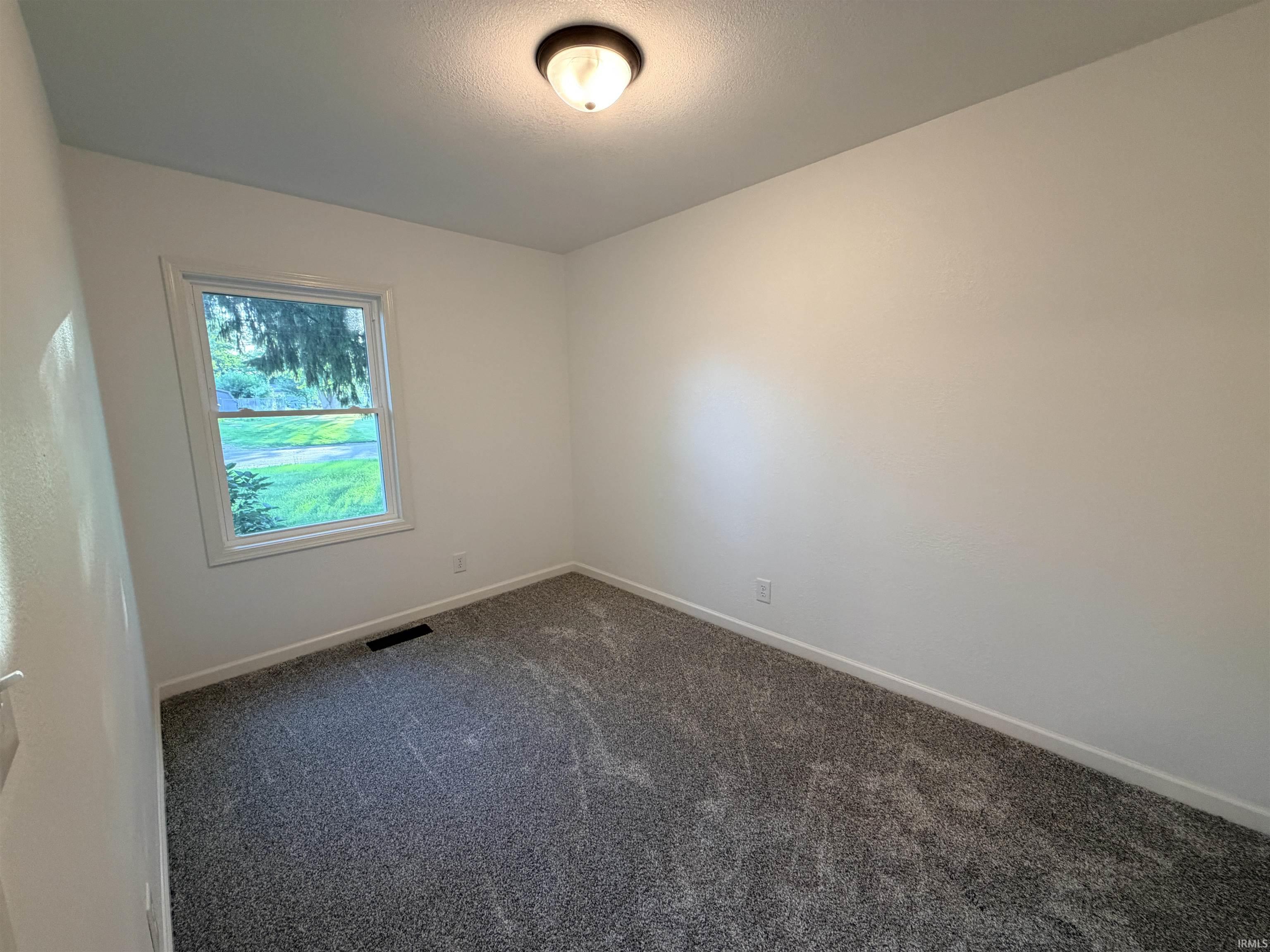 Neutral-toned room featuring a double-hung window, fresh white walls, and new gray carpeting