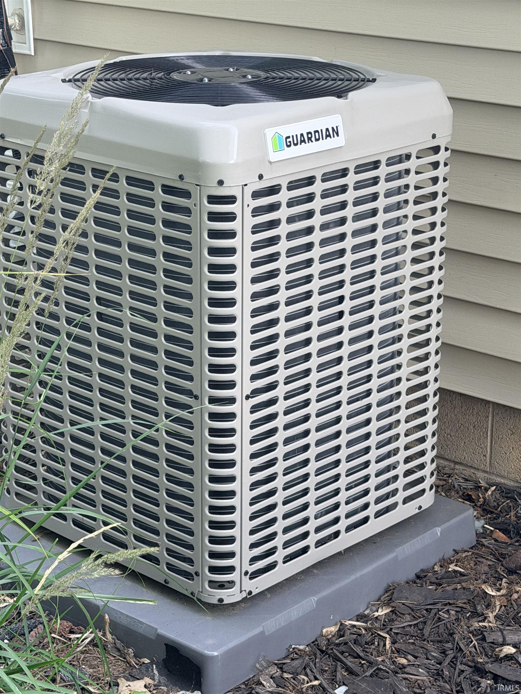 Exterior air conditioning unit on a solid grey pad, positioned against horizontal siding