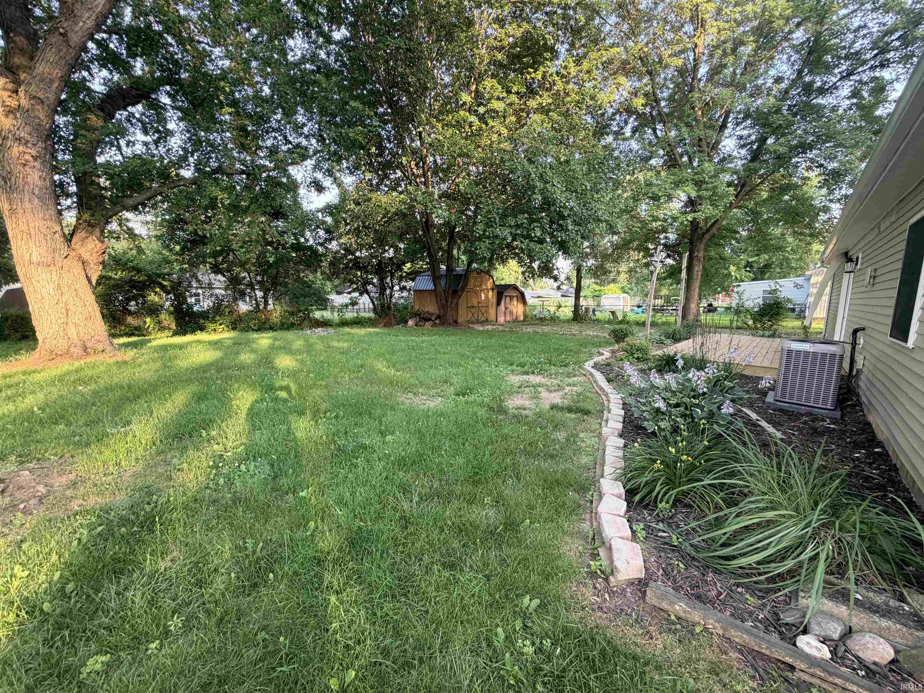 Spacious backyard featuring a large tree, green lawn, and a wood storage shed
