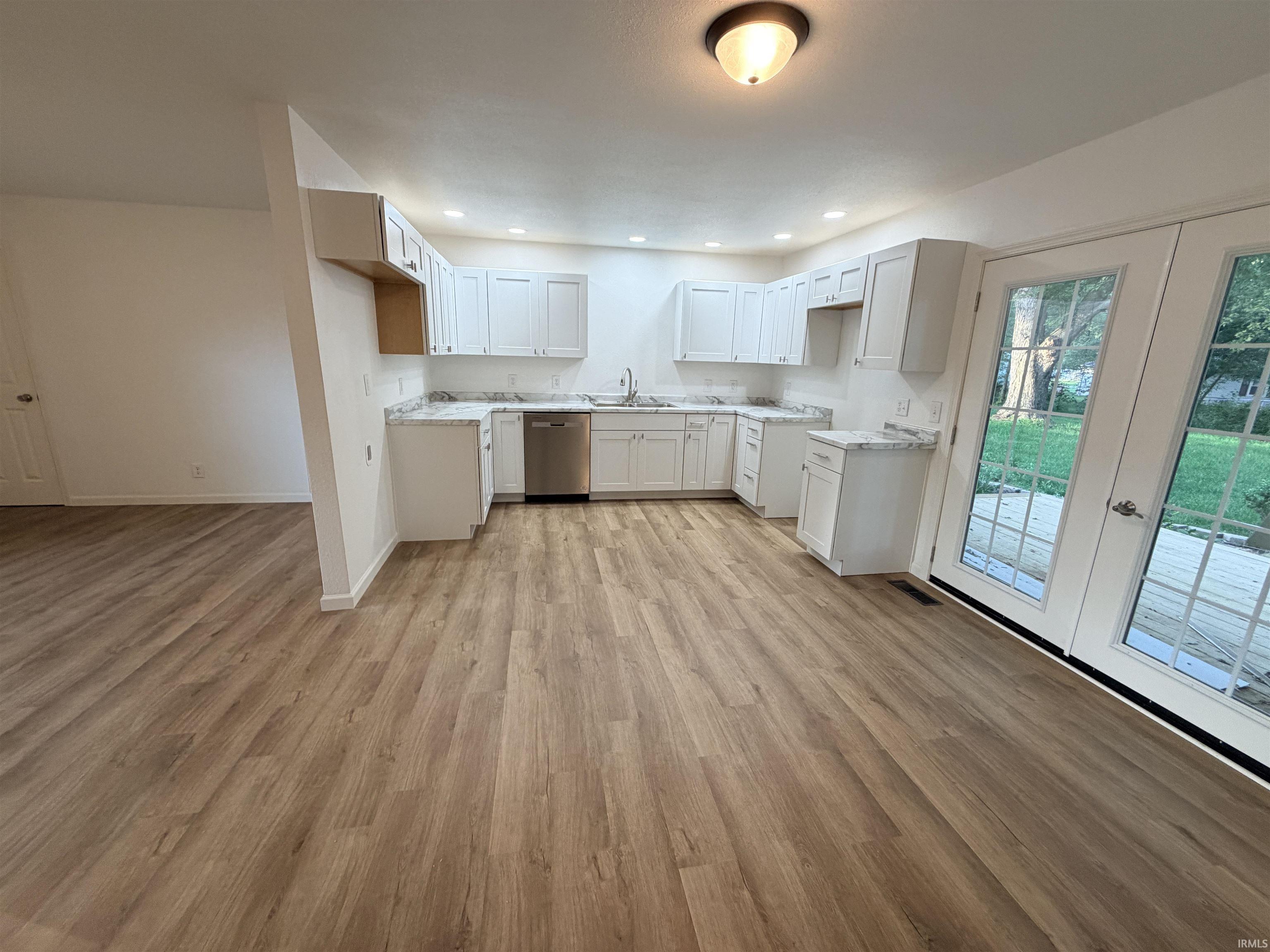 Kitchen featuring white cabinetry, light-toned countertops, stainless steel dishwasher, and wood-finish flooring