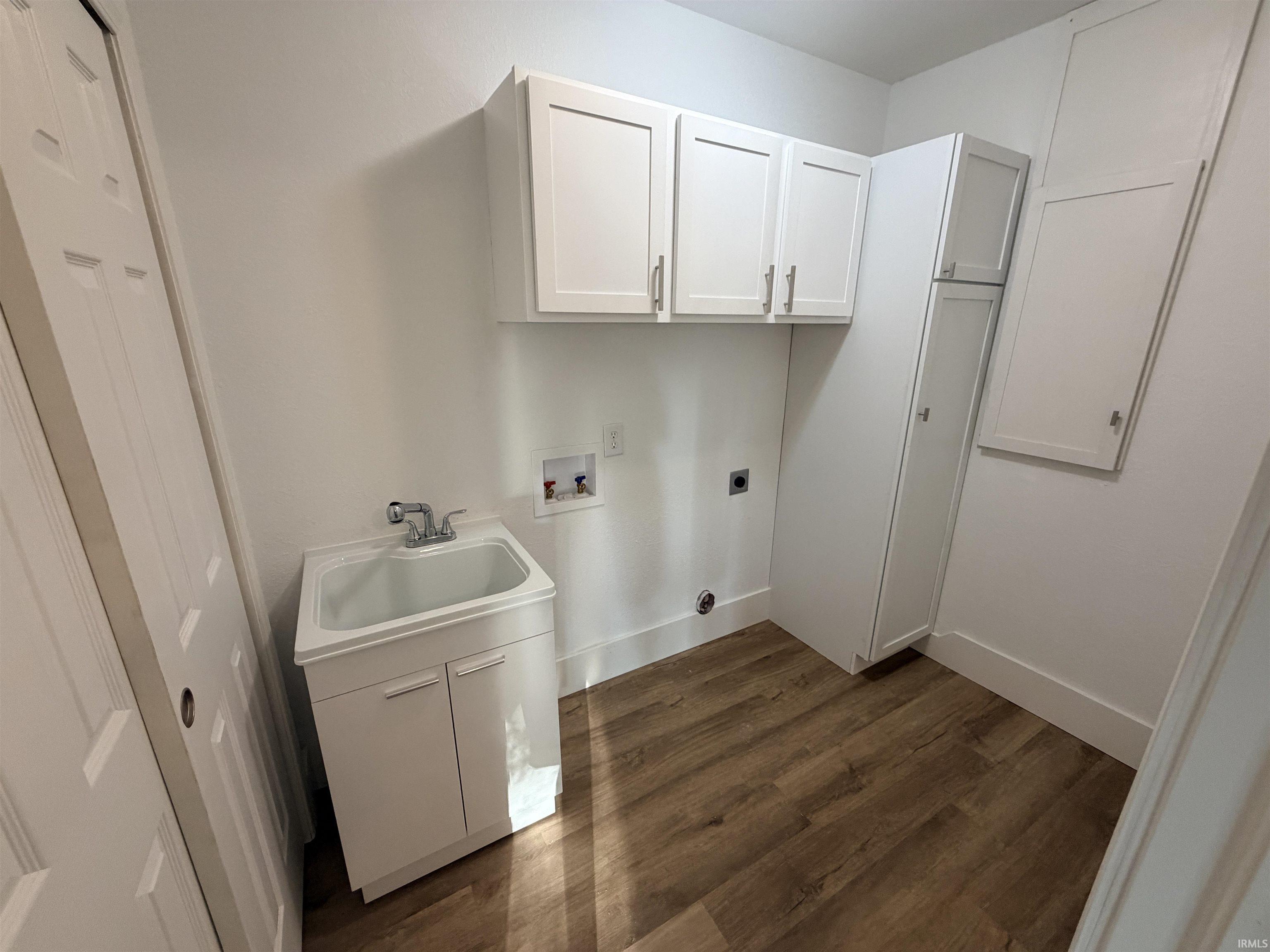 Laundry area featuring wood-finish flooring, white cabinetry, a utility sink with a faucet, and appliance hookups