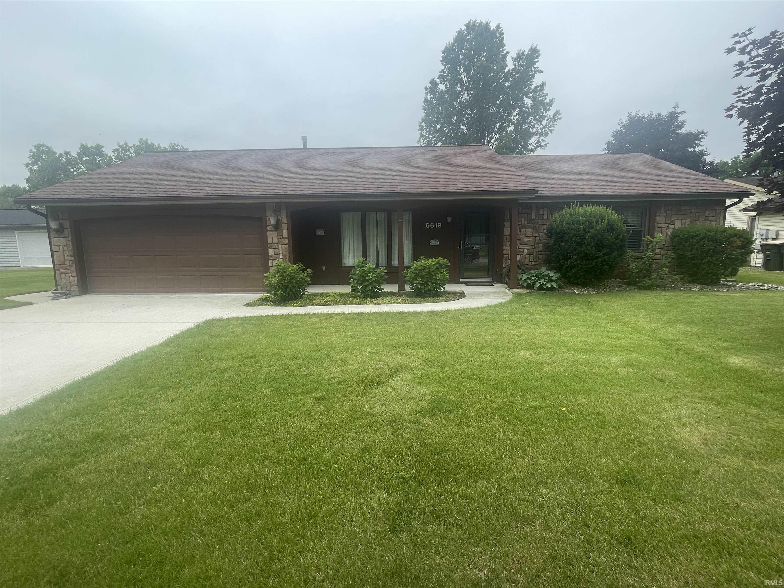 Ranch-style residence featuring a prominent front lawn, stone facade accents, an attached garage, a paved driveway, and a curved concrete walkway leading to the front entry