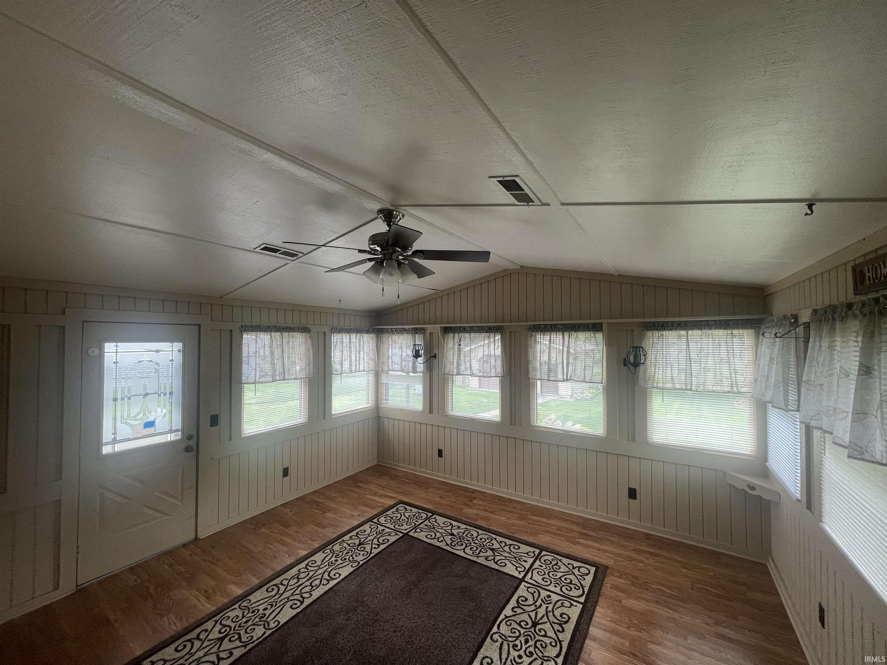 Sunroom featuring wood-finish flooring, numerous windows, a ceiling fan, and a white paneled door with decorative glass