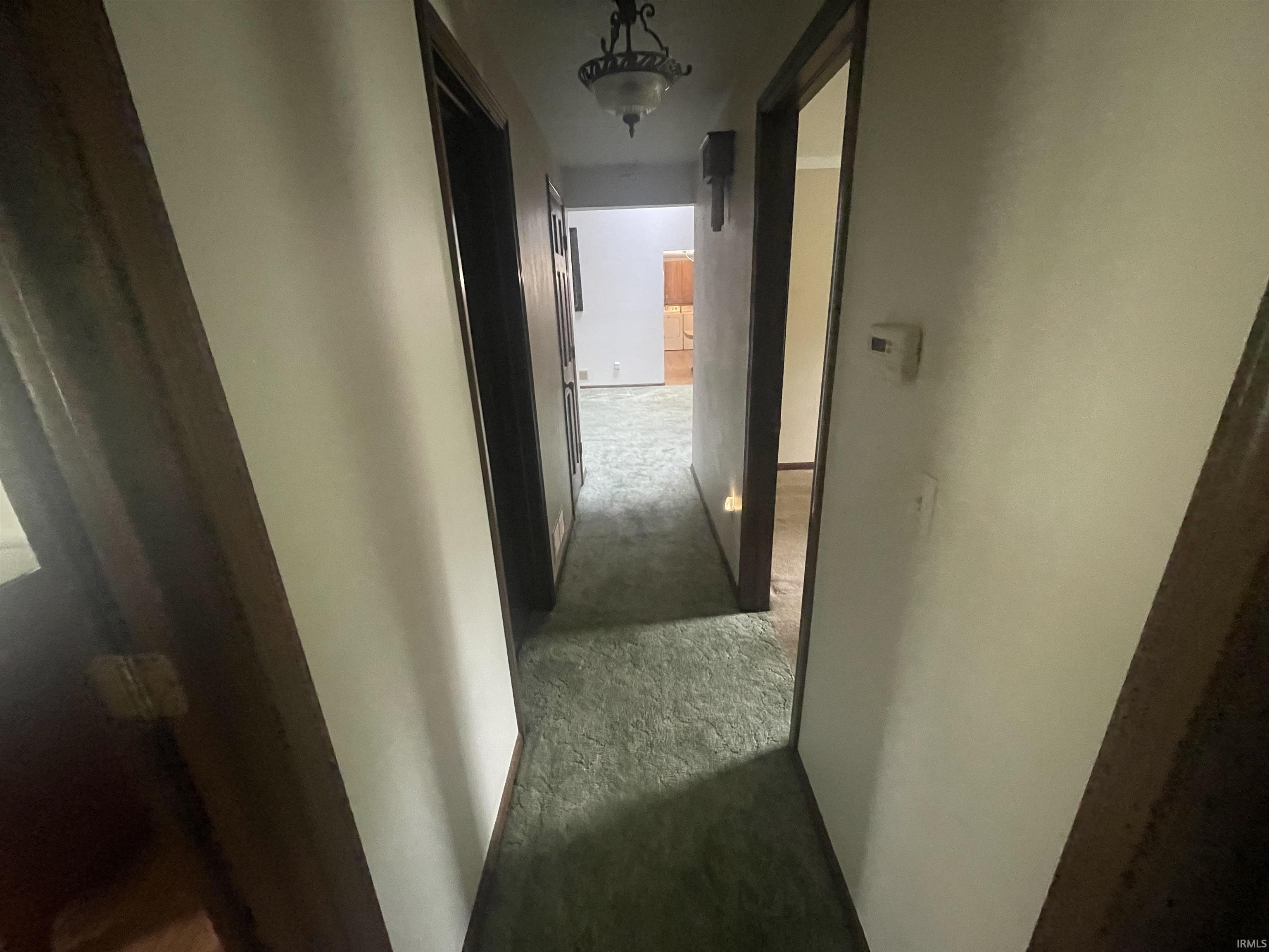Hallway featuring green carpeting, white walls, and dark wood-finish trim