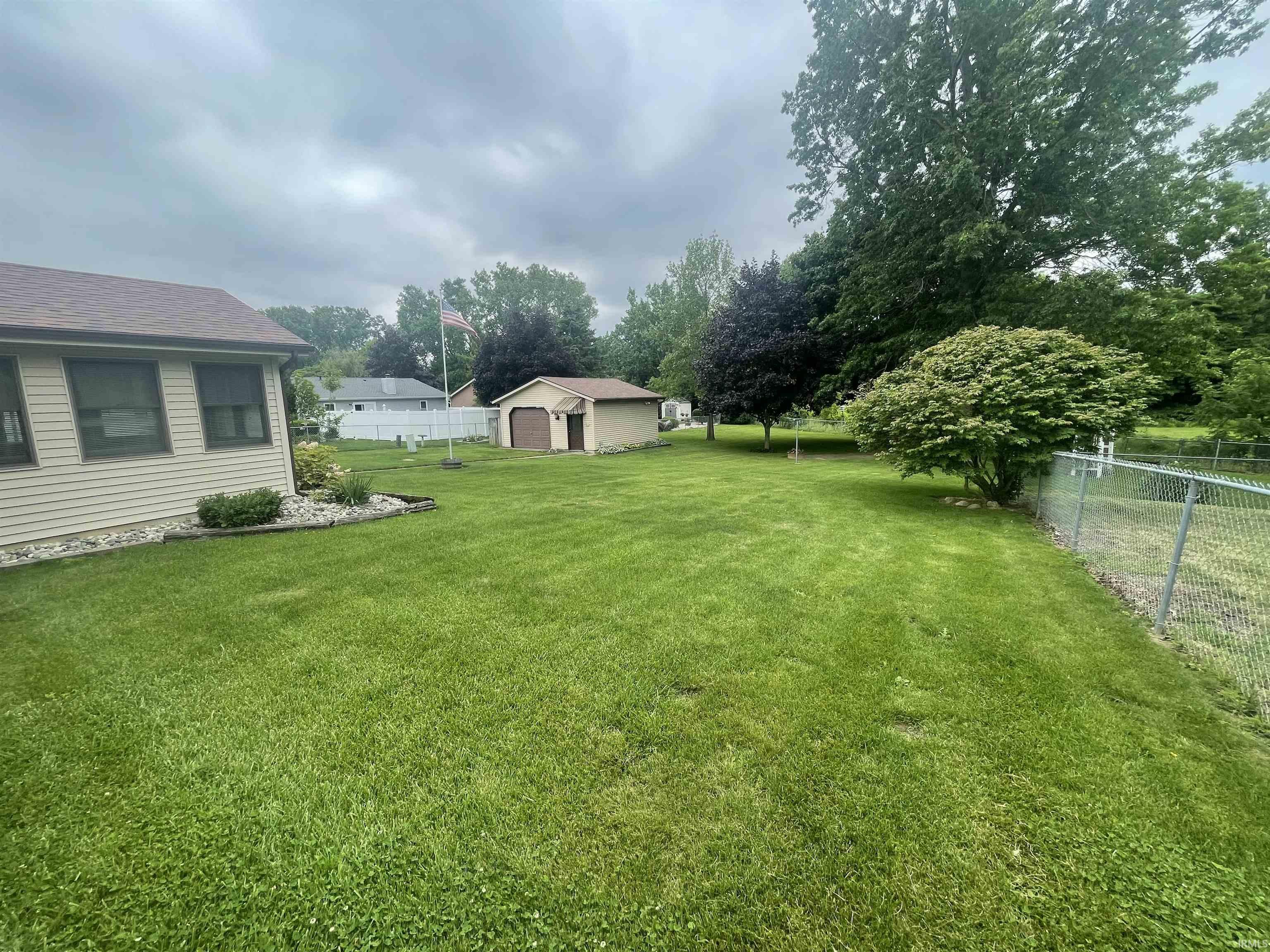 Spacious backyard featuring a chain-link fence, mature trees, and a detached shed with a garage door