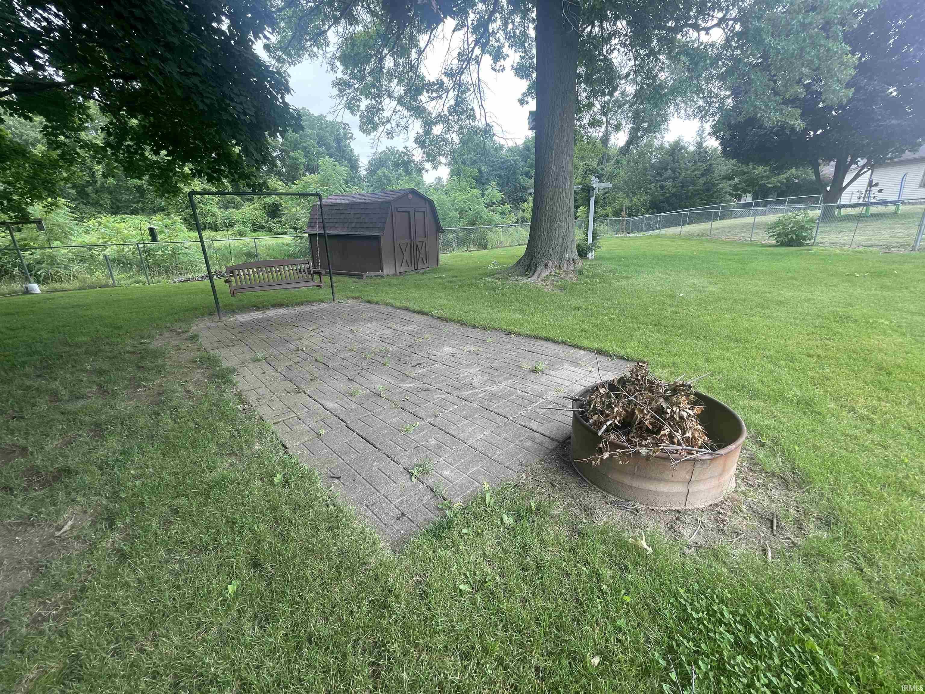 Expansive backyard featuring a paver patio with a swing structure and a metal fire pit