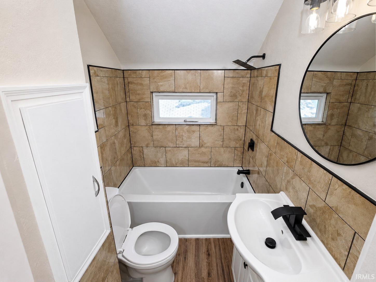 Bathroom featuring a white tub, light-toned wall tiling, and wood-finish flooring