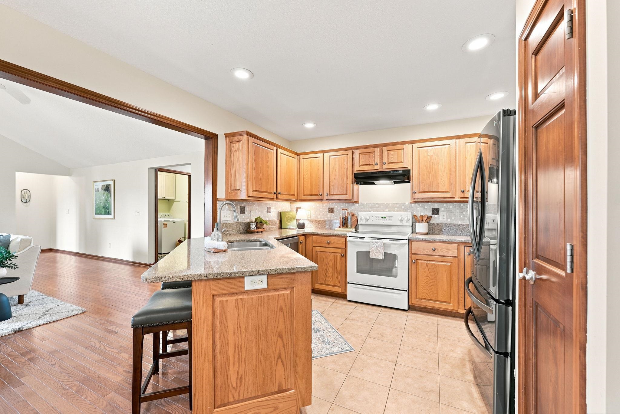 Kitchen featuring light wood cabinetry, stone countertops, stainless steel refrigerator, white range, and recessed lighting