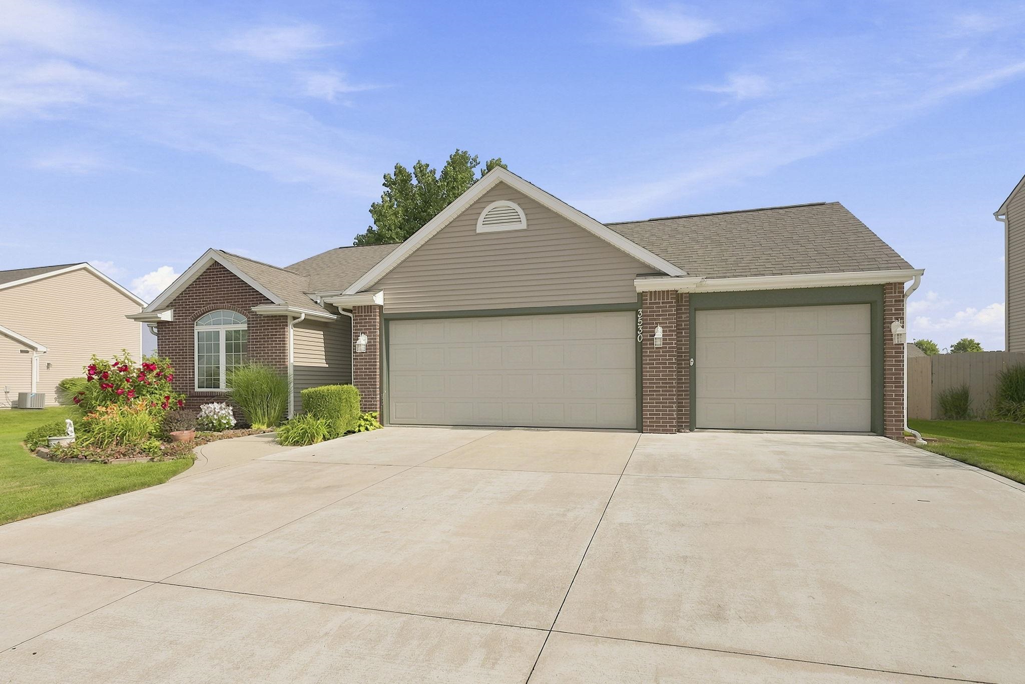 Brick and siding exterior featuring an arched window, a two-car garage, a single-car garage, and a concrete driveway