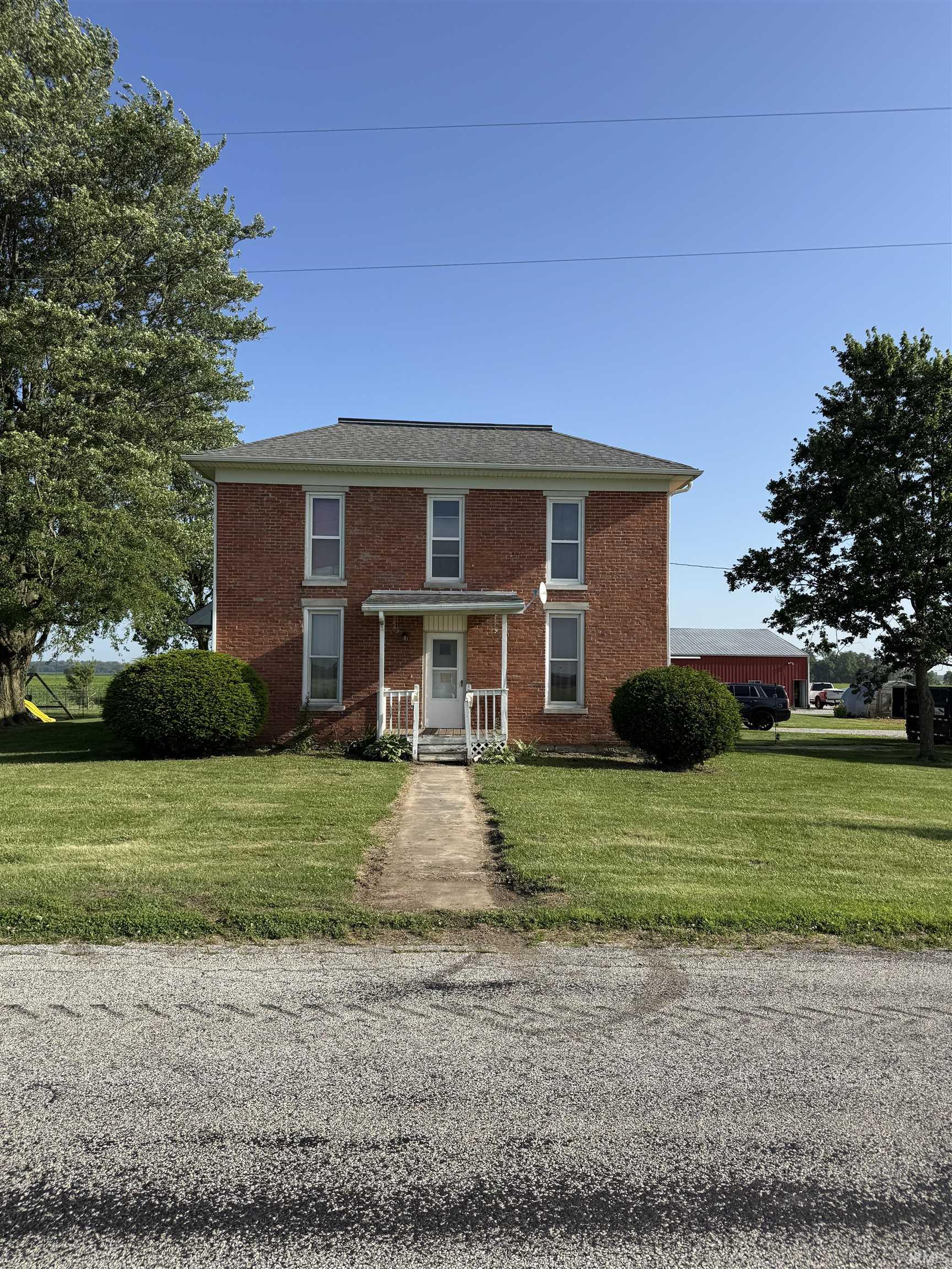 Brick exterior residence featuring a front porch with white railings, a concrete path, and a shingled roof