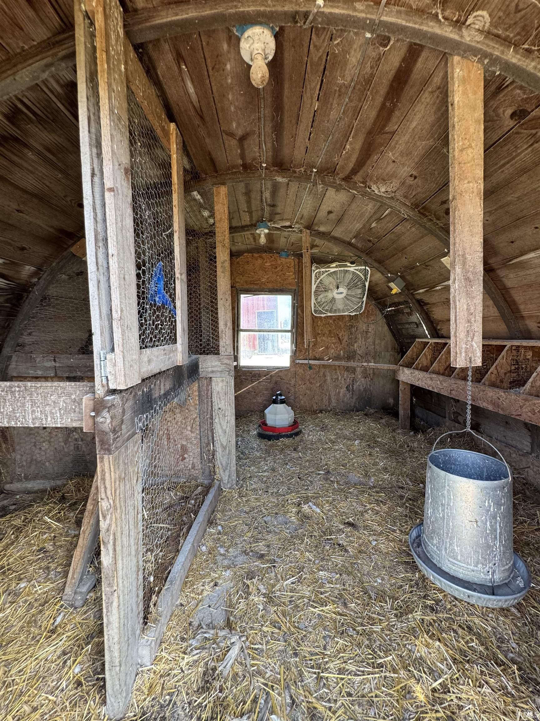 Interior of an agricultural structure featuring a curved wood-plank ceiling, wood-frame partitioning with wire mesh, and a small window