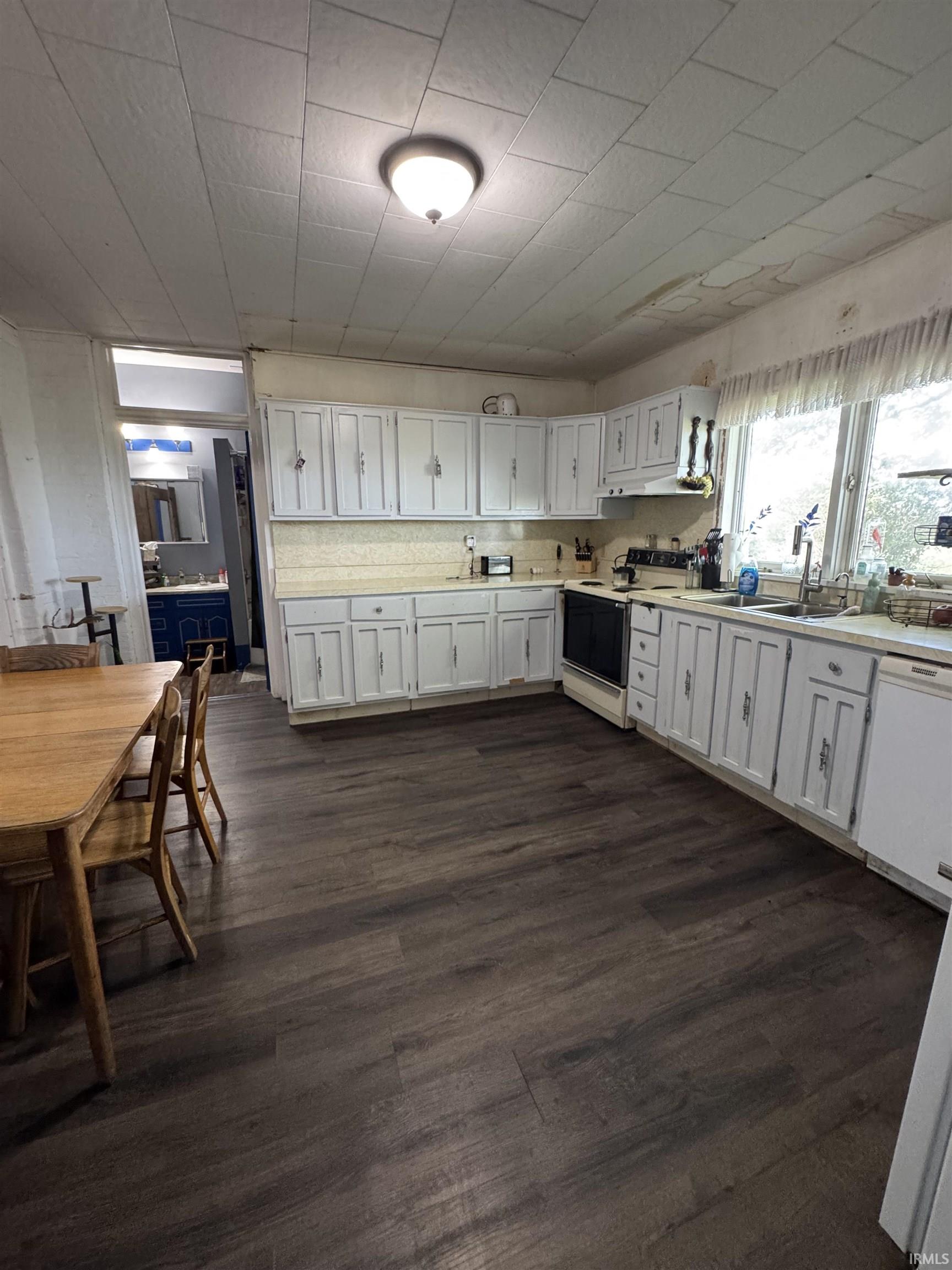 Kitchen featuring wood-finish flooring, white cabinetry, light-toned countertops, a stainless steel range, and a window with a valance
