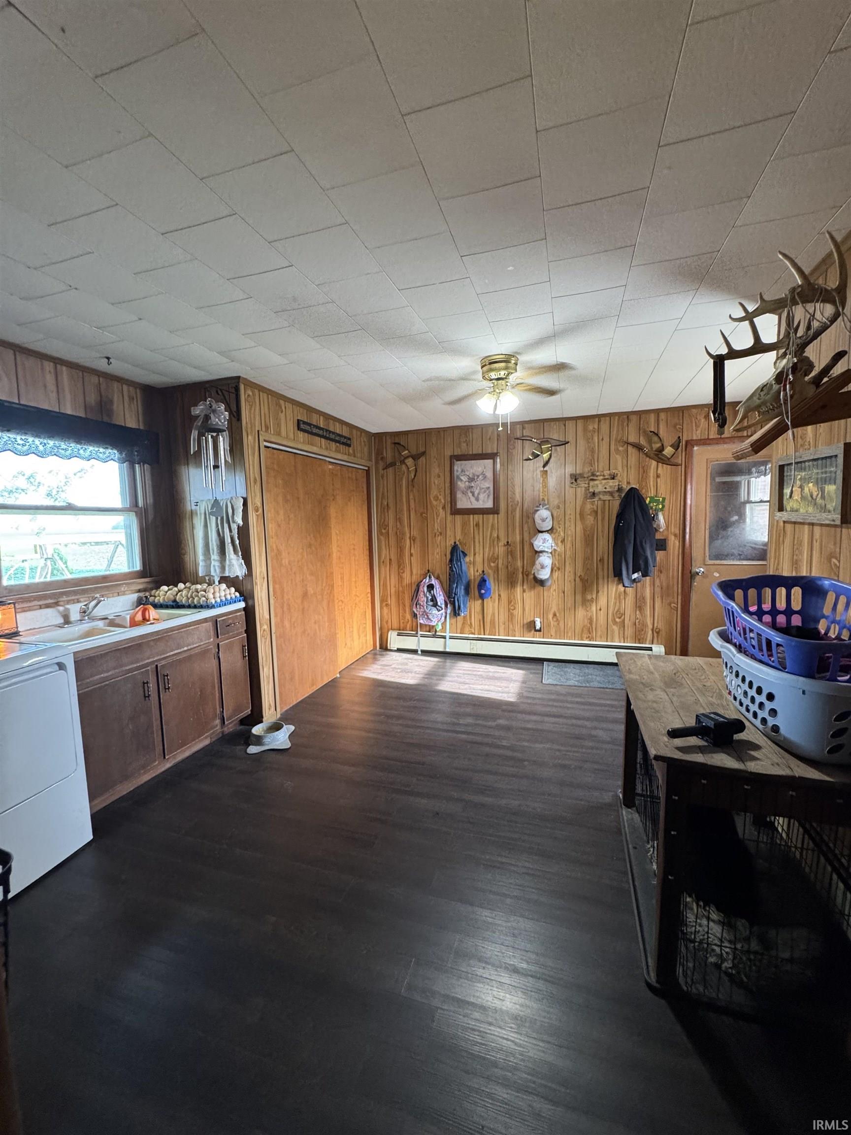 Mudroom/Laundry Room area featuring dark wood-finish flooring, wood paneling, and a white ceiling with a rectangular tile pattern and closet storage.