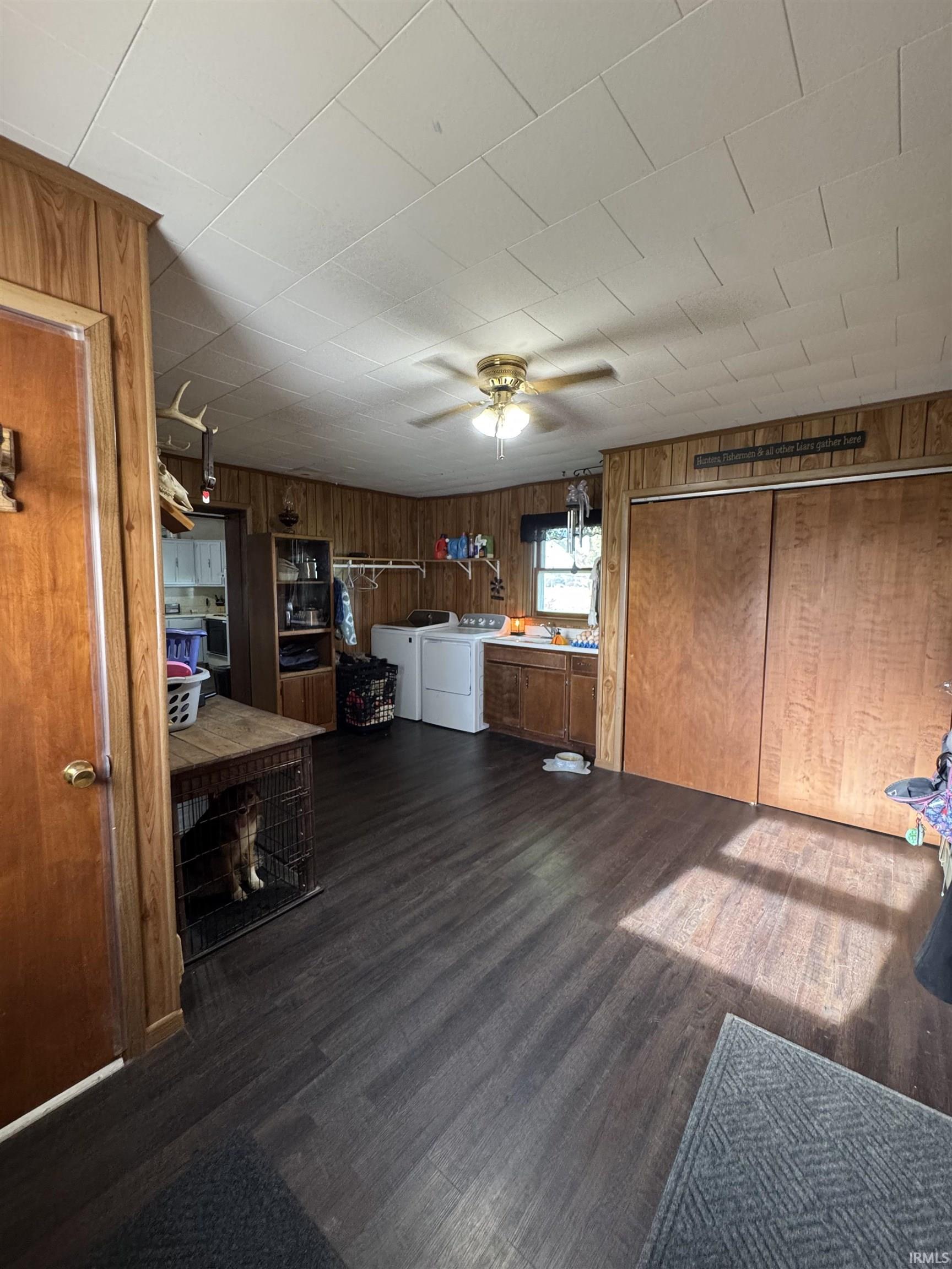 Spacious utility room featuring wood-finish flooring, wood paneling, and a ceiling fan and closet storage.