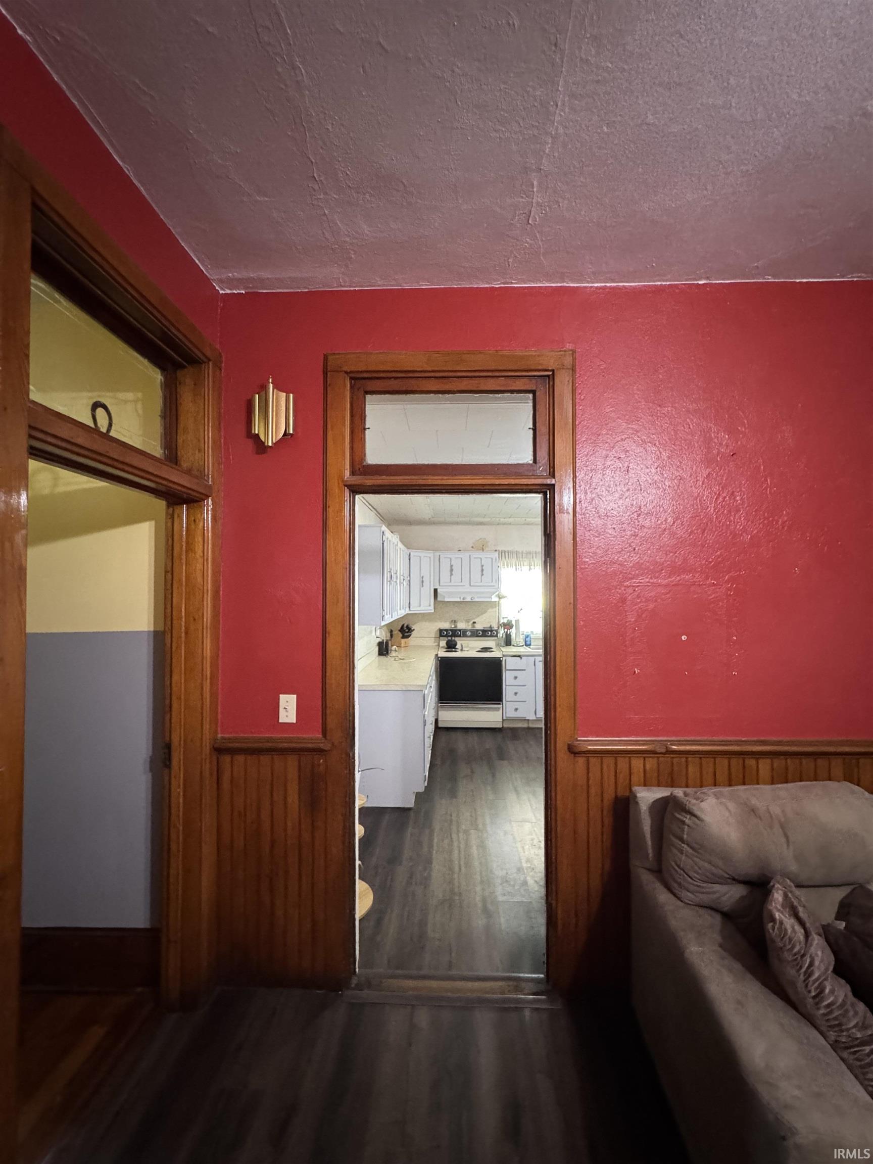 Passageway with dark wood-finish flooring, red wall paint, and wood paneling, featuring a clear line of sight to a kitchen with white cabinetry and light countertops