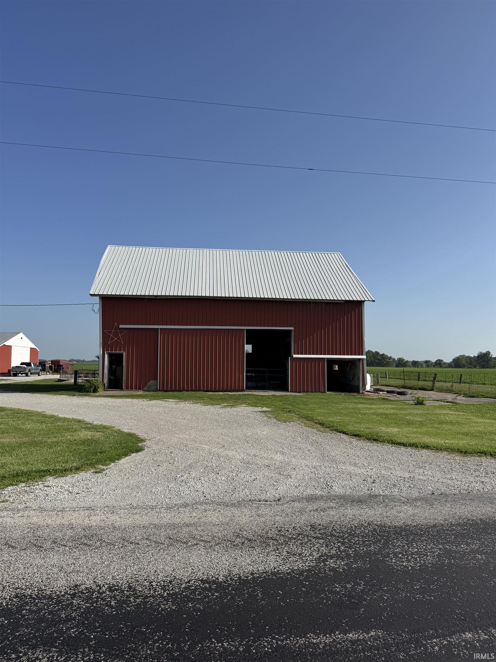Red barn with a corrugated metal roof, gravel driveway, and surrounding green lawn