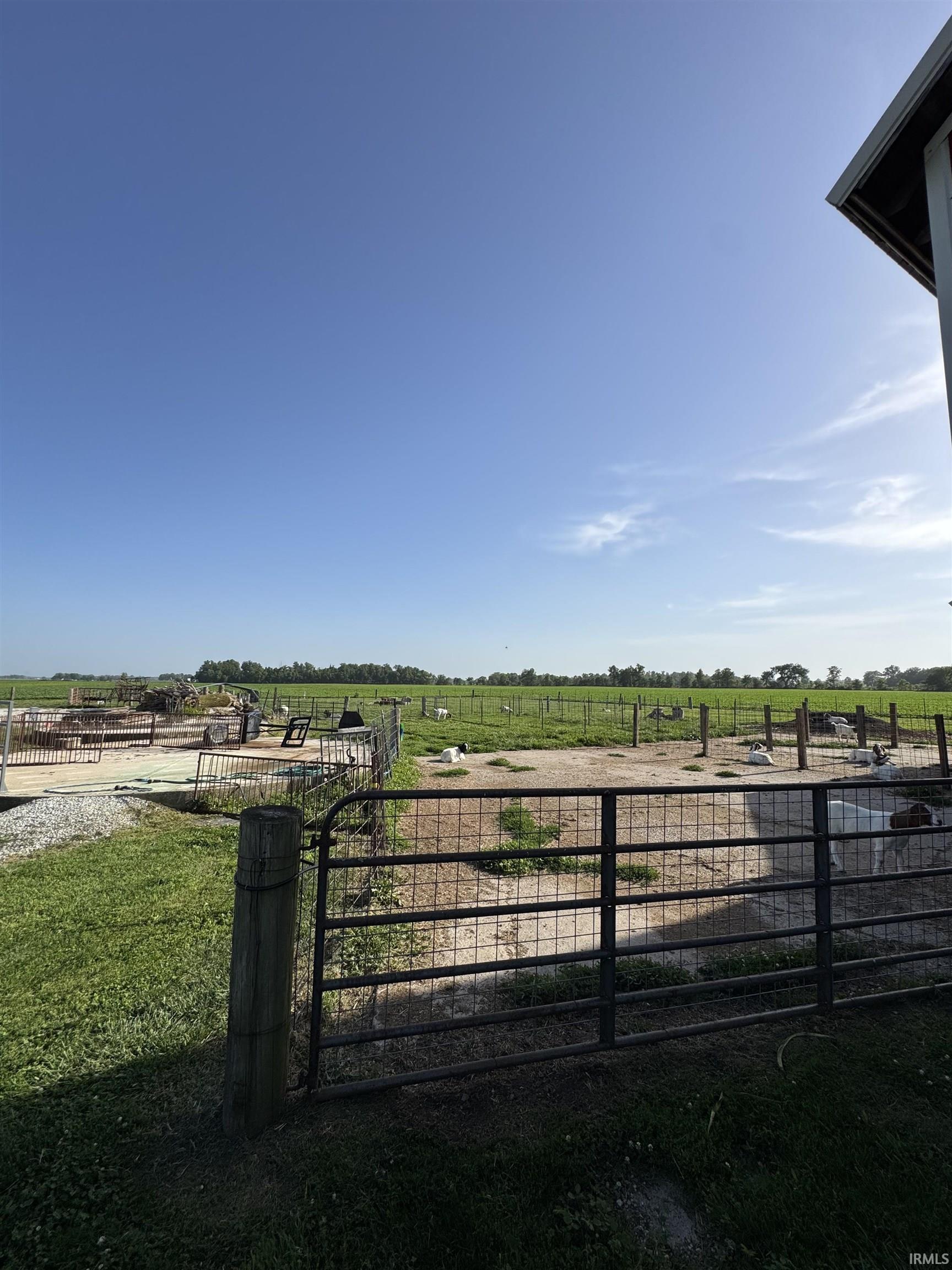 Expansive agricultural property featuring a metal gate, multiple fenced enclosures, and vast open fields extending to the tree line