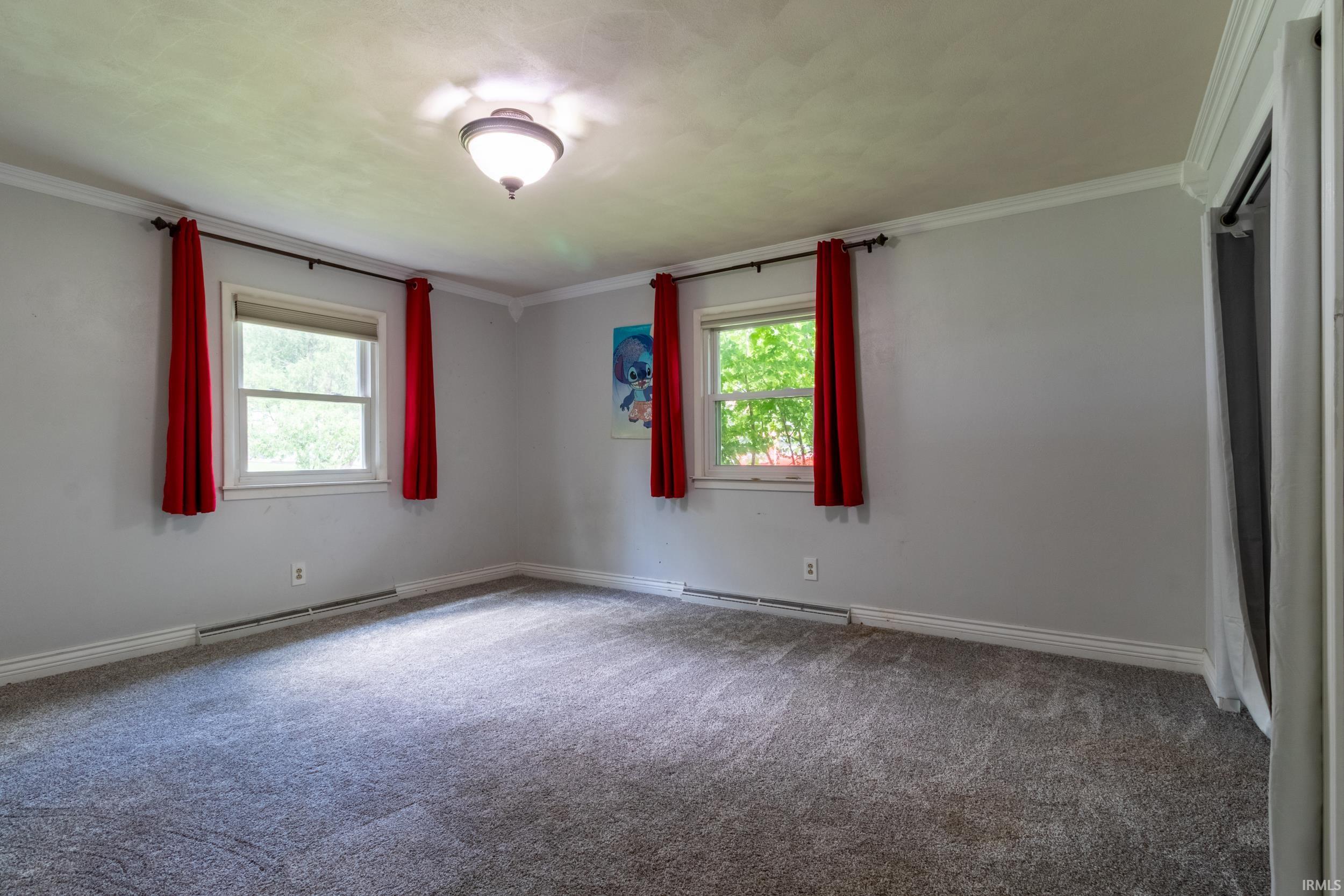 Carpeted room with a ceiling-mounted light fixture, two windows, and crown molding