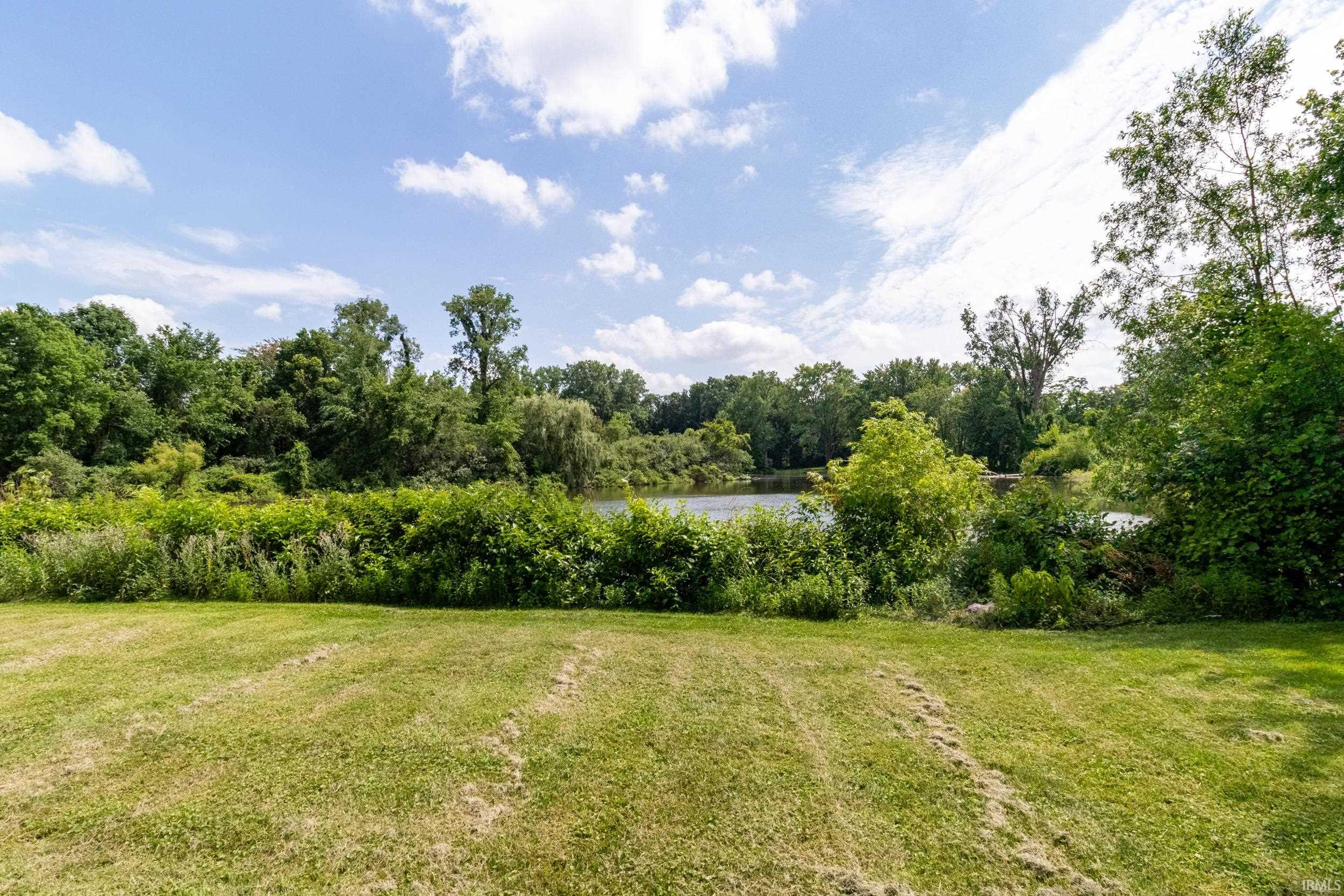 Expansive green lawn bordering a body of water, framed by lush mature trees and dense foliage