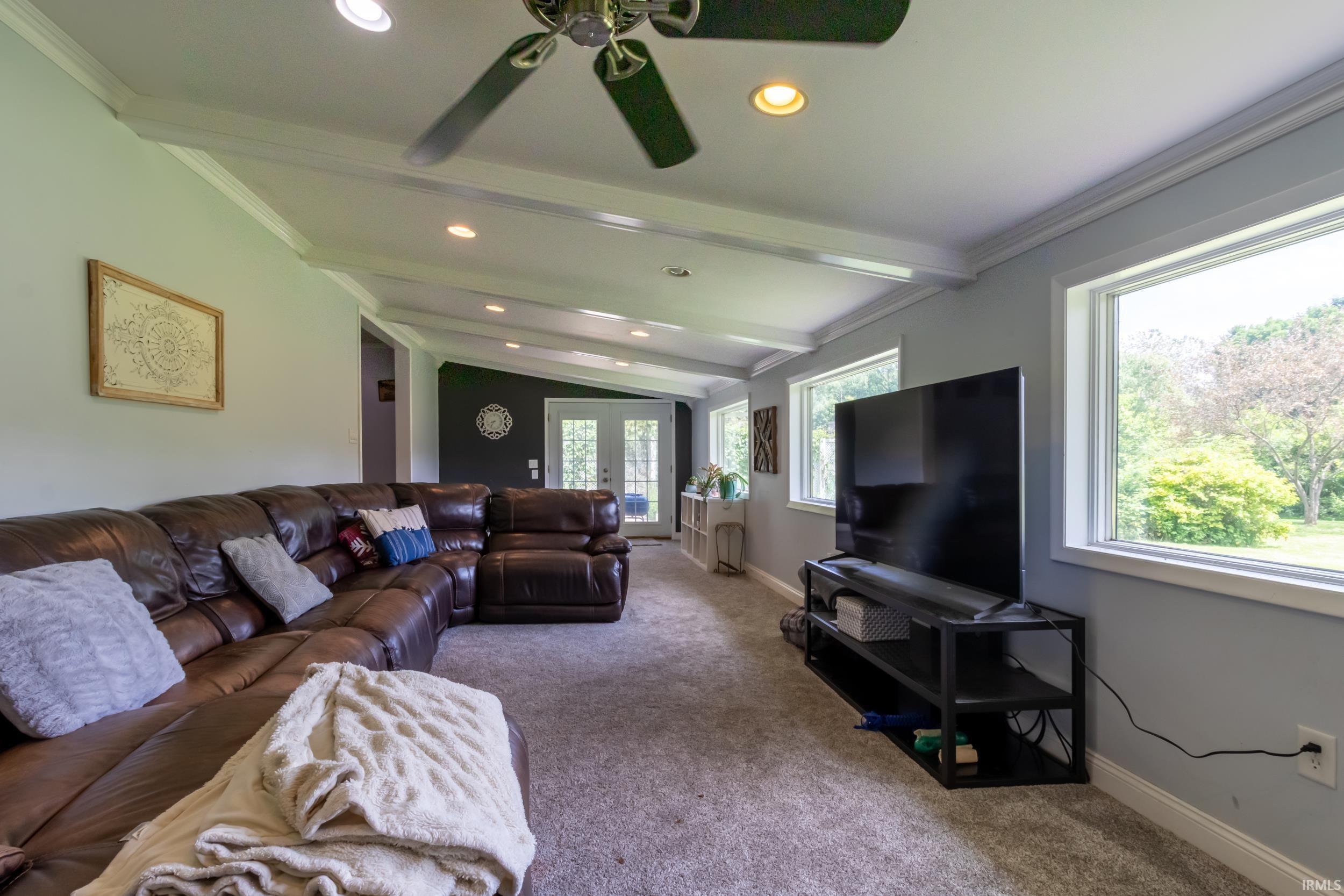 Spacious living area featuring exposed white beams, recessed lighting, and a ceiling fan