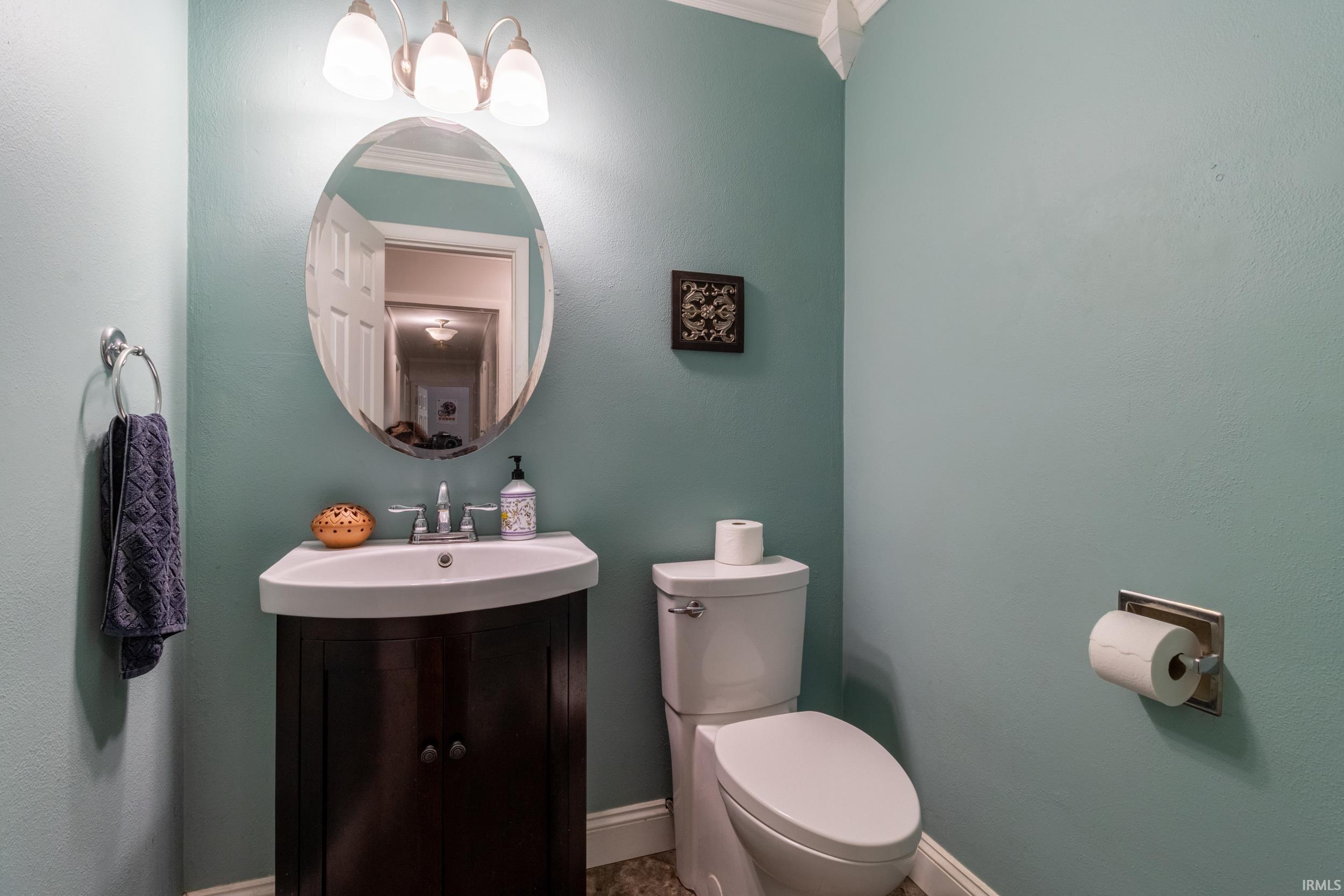 Bathroom featuring a dark wood-finish vanity with an integrated white sink, an oval mirror, and a three-light vanity fixture