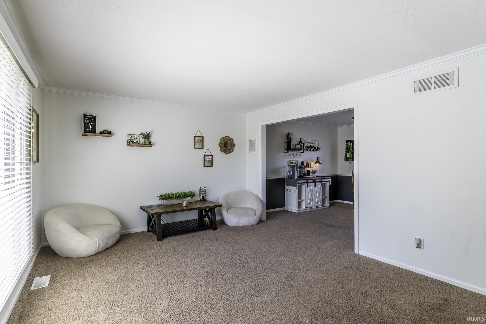 Carpeted living space featuring white walls and crown molding