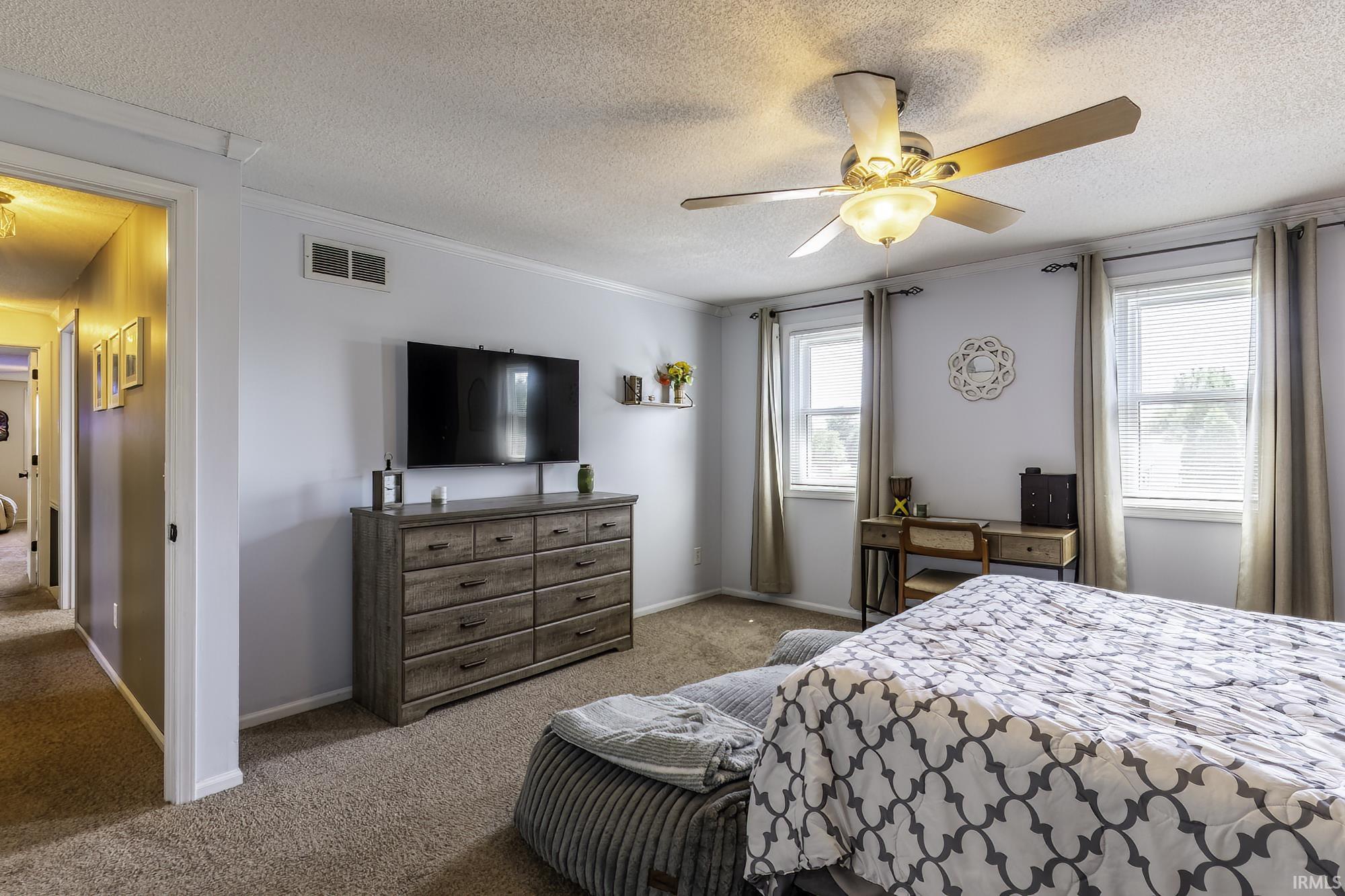 Carpeted bedroom with a ceiling fan light fixture, two windows with blinds, crown molding, and a built-in wall niche