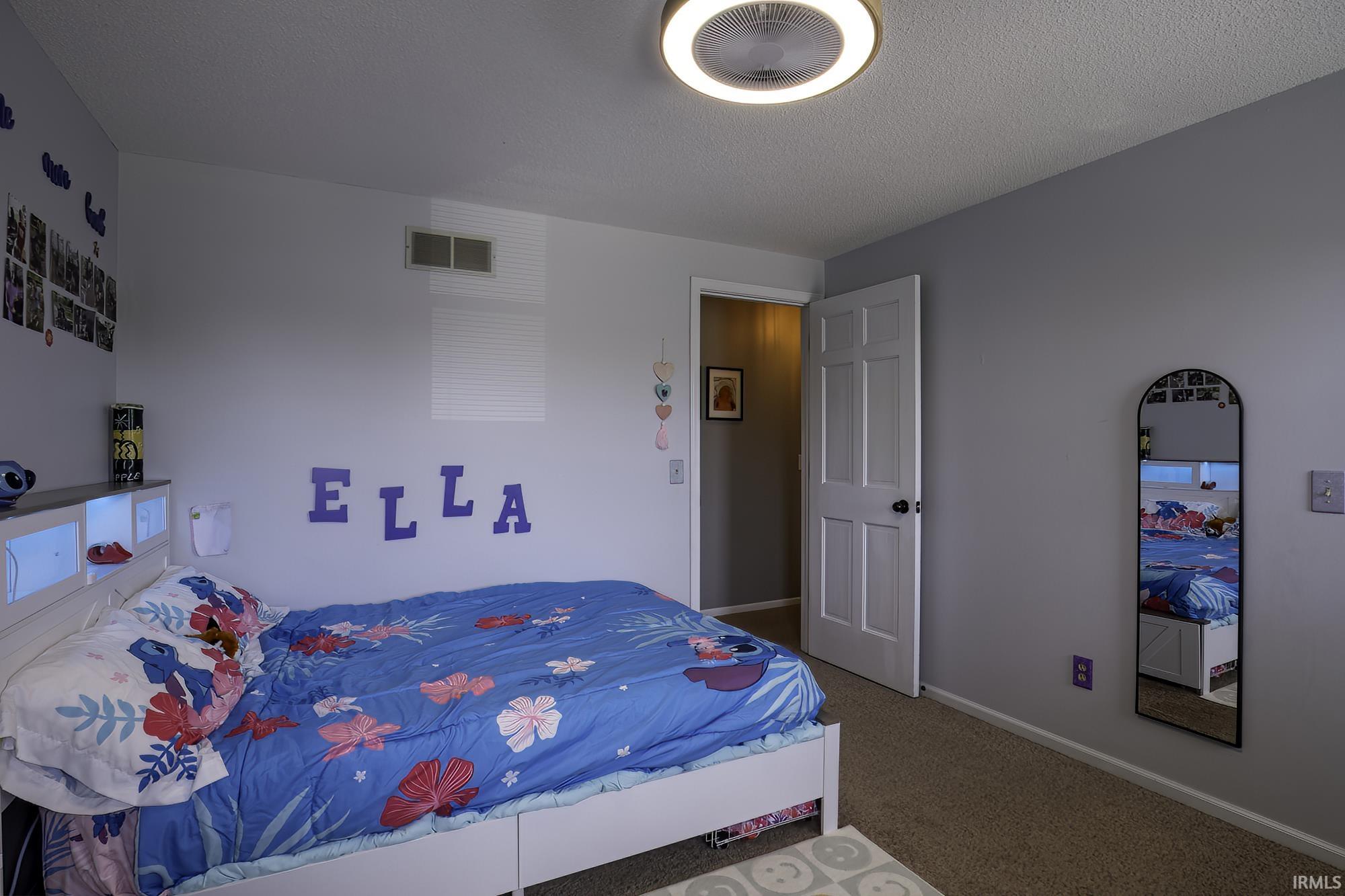 Carpeted room featuring a white paneled door with black hardware, a ceiling-mounted light fixture, and a built-in headboard with integrated lighting
