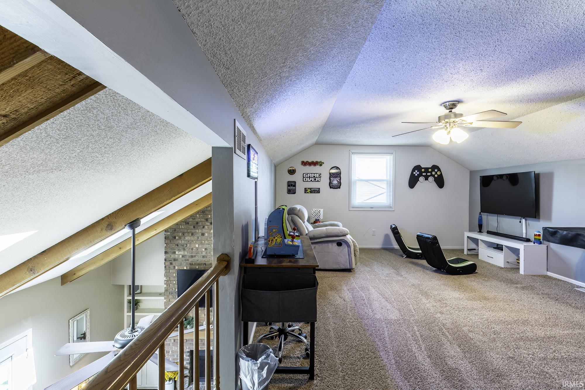 Spacious loft area featuring sloped ceilings, a ceiling fan with integrated lighting, and a window for natural illumination