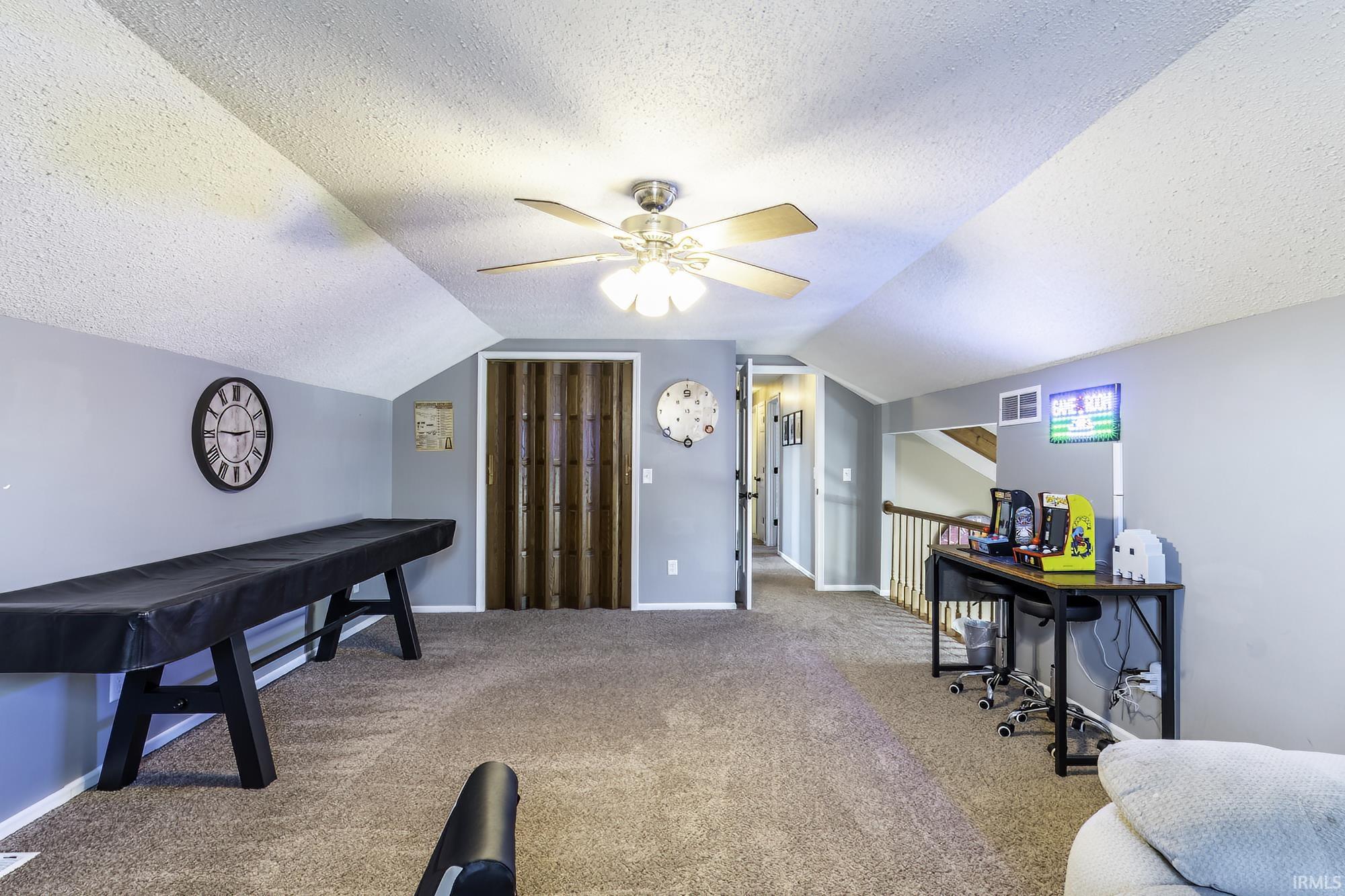 Carpeted attic space featuring a ceiling fan, sloped ceilings, light gray walls, and a wood-look accordion door