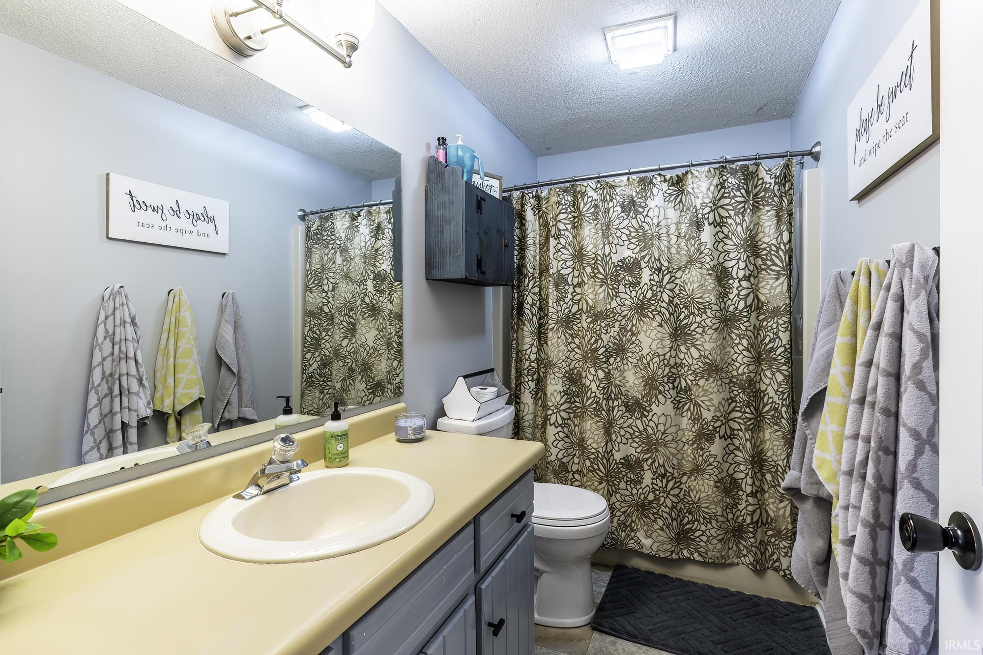 Bathroom featuring a vanity with an integrated sink, a large wall-mounted mirror, a shower-tub combination with a floral shower curtain, and overhead lighting