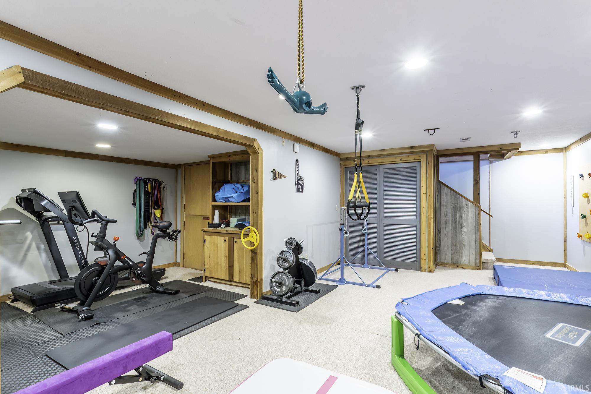 Recreational space featuring exposed wood beams, recessed lighting, carpet flooring, a built-in wood cabinet, and wood-paneled walls