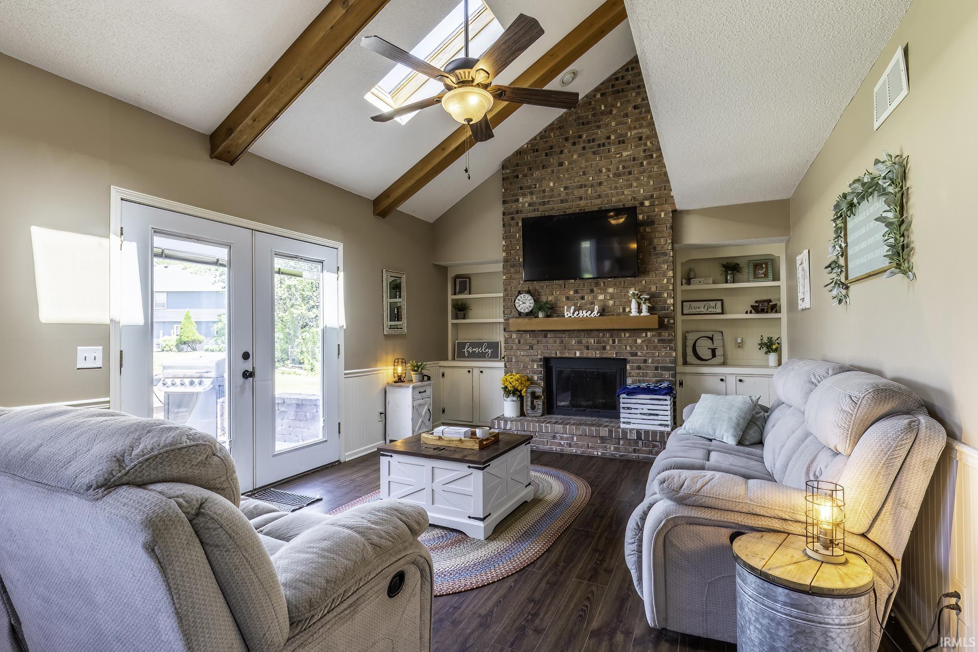 Vaulted ceiling living room featuring exposed wood beams and a central ceiling fan with integrated lighting