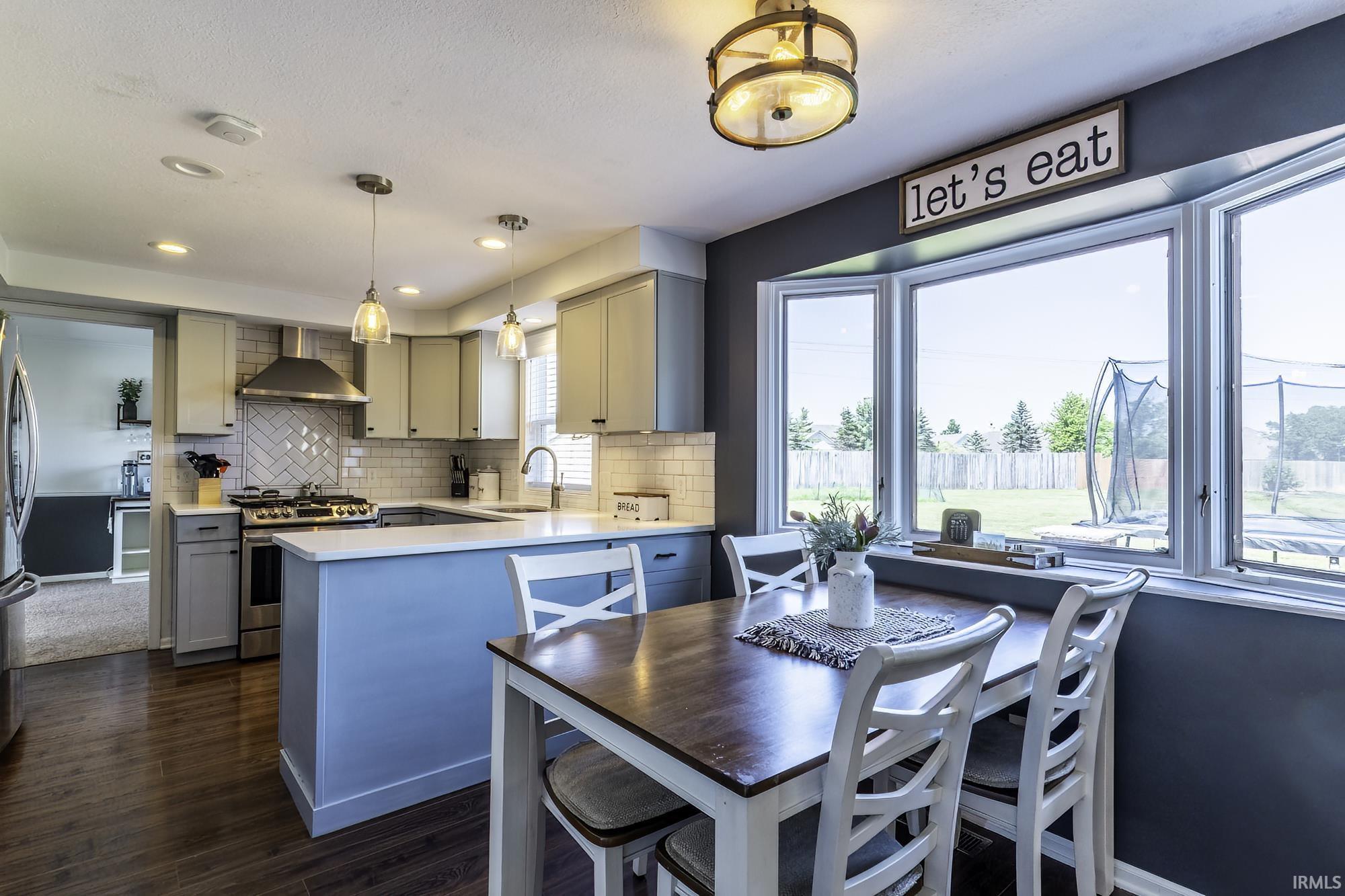 Kitchen featuring wood-finish flooring, light gray cabinetry, stainless steel appliances, a subway tile backsplash, and a large bay window