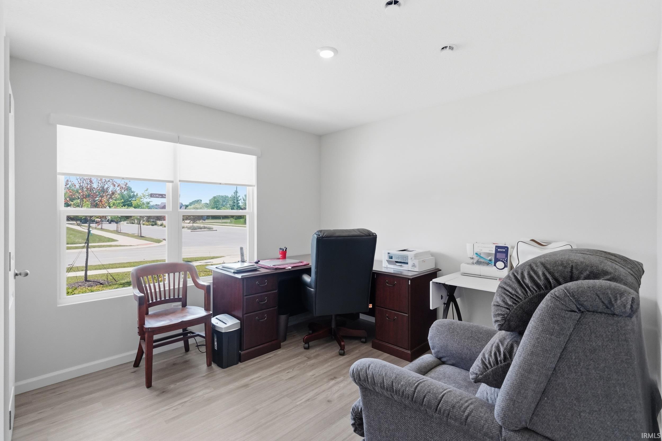 Bright room featuring light wood-finish flooring, white walls, and a large window with roller shades