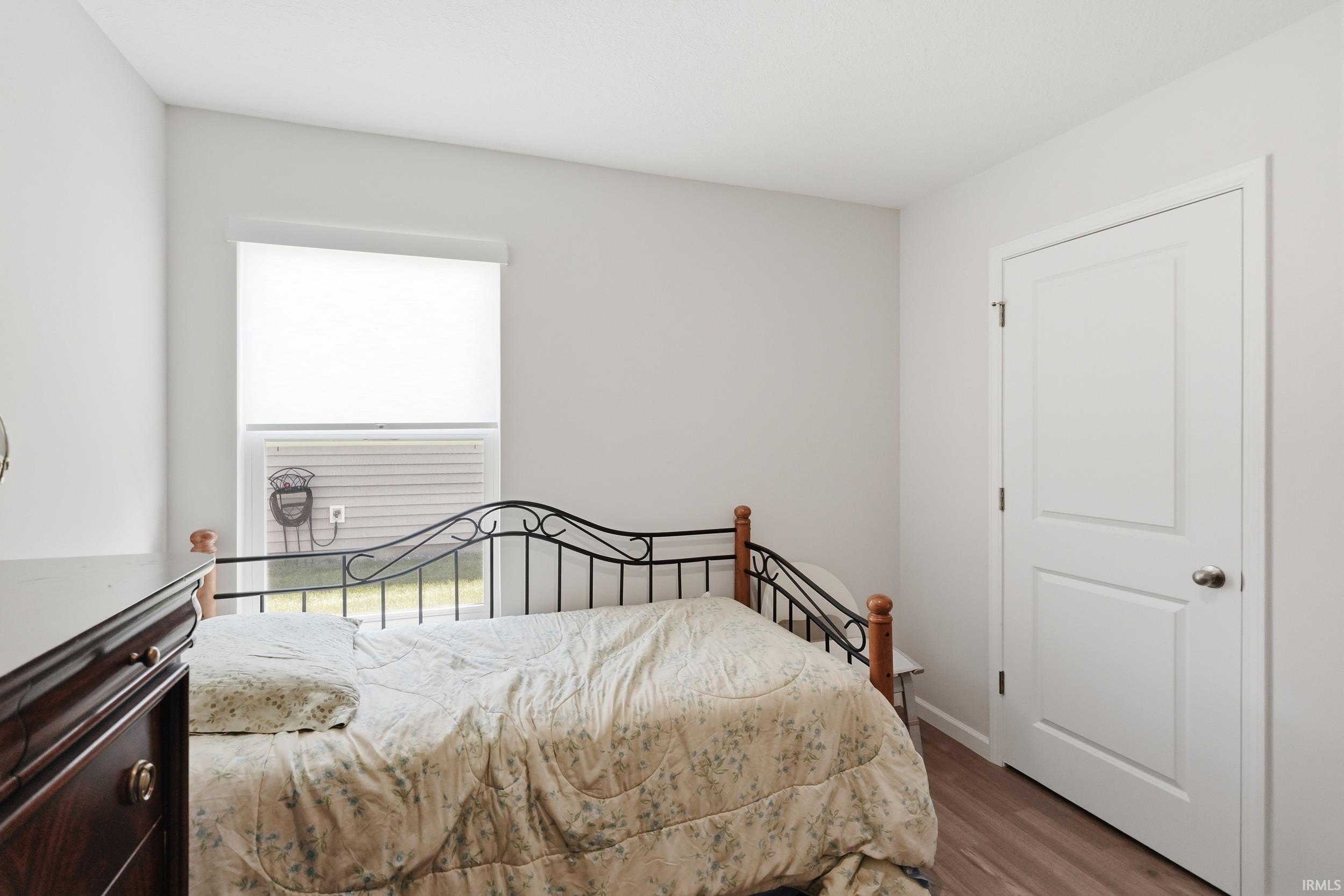 Neutral-toned interior featuring wood-finish flooring, a white paneled door, and a window with a roller shade