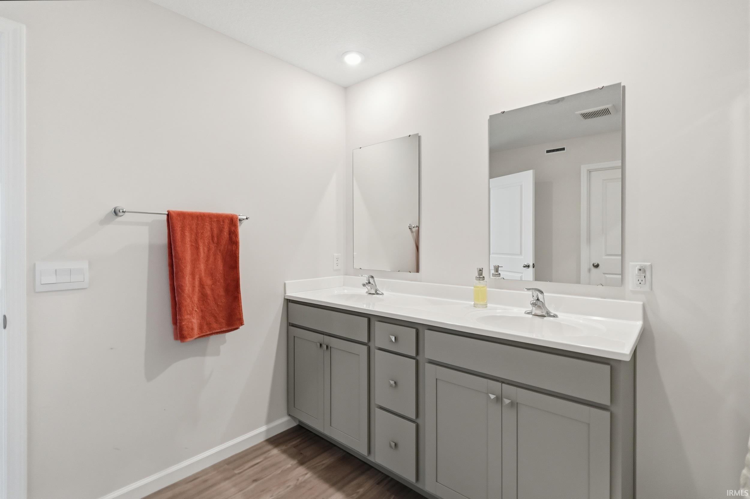 Dual sink vanity featuring a light countertop, gray cabinetry, chrome fixtures, and wood-finish flooring