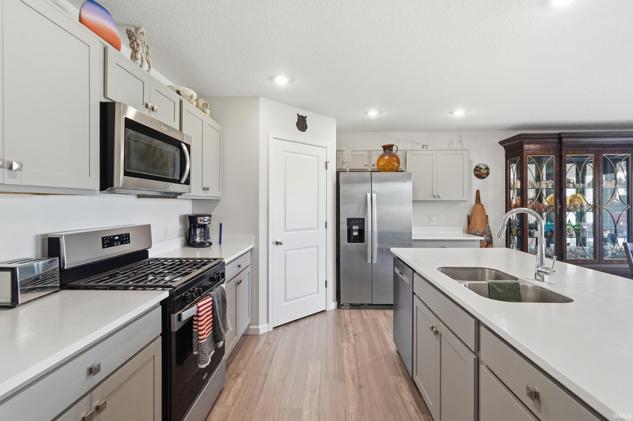 Kitchen featuring light gray cabinetry, stainless steel appliances, a center island with a double basin sink, white countertops, and wood-finish flooring