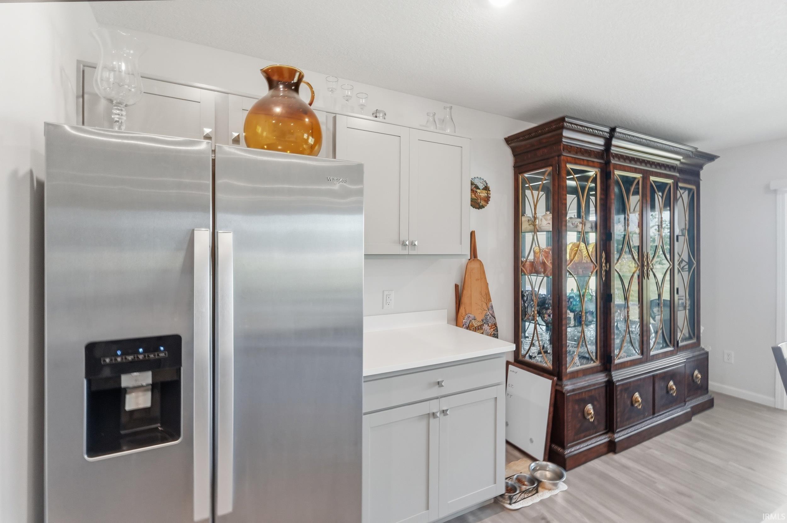 Stainless steel side-by-side refrigerator, light gray cabinetry with brushed nickel hardware, light-toned countertops, and wood-finish flooring