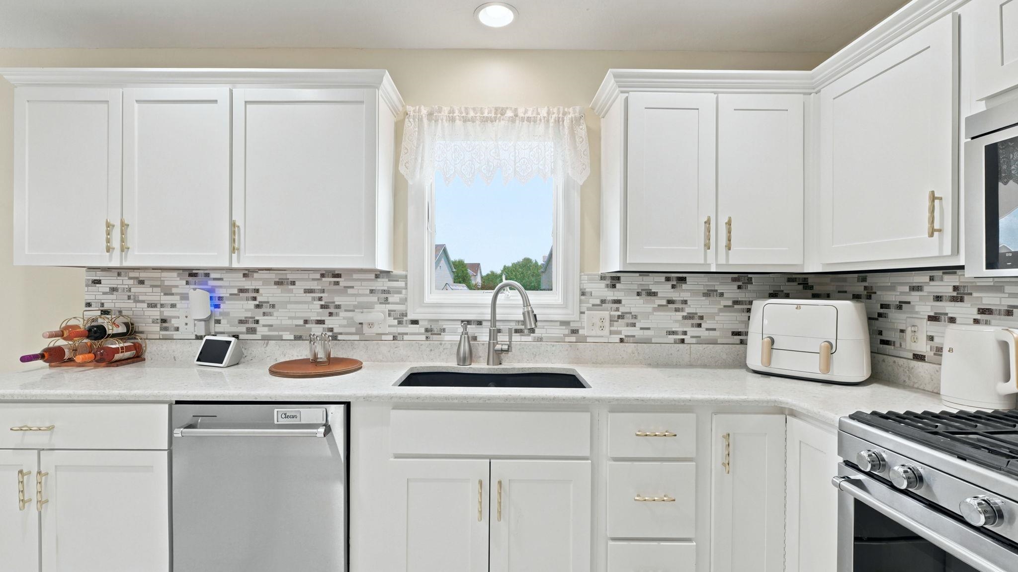 Contemporary kitchen featuring white cabinetry, light-toned countertops, a mosaic tile backsplash, stainless steel appliances, and an undermount sink