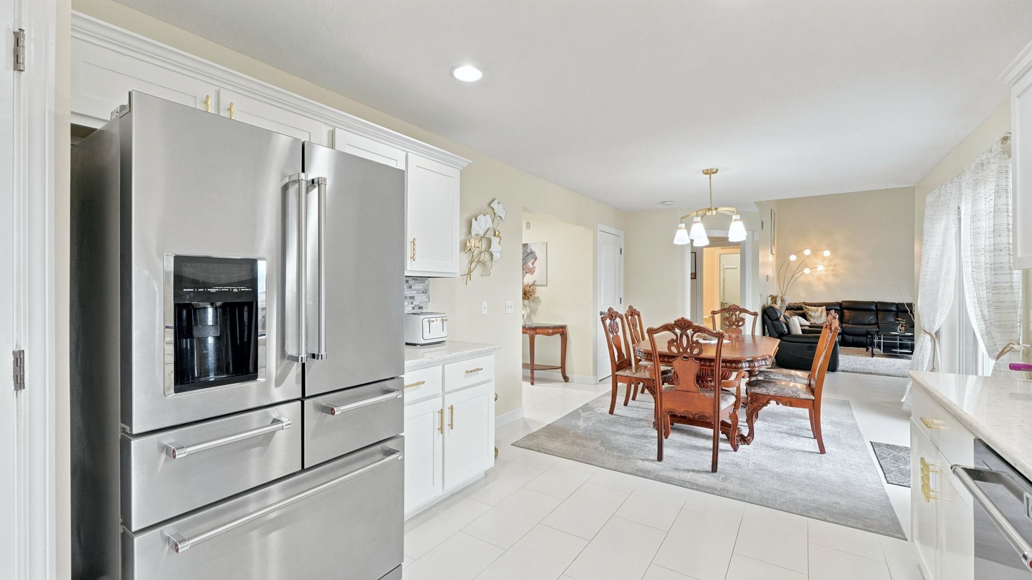 Spacious kitchen and dining area featuring a stainless steel French door refrigerator with an ice and water dispenser, white cabinetry with gold-tone hardware, and light-toned tile flooring