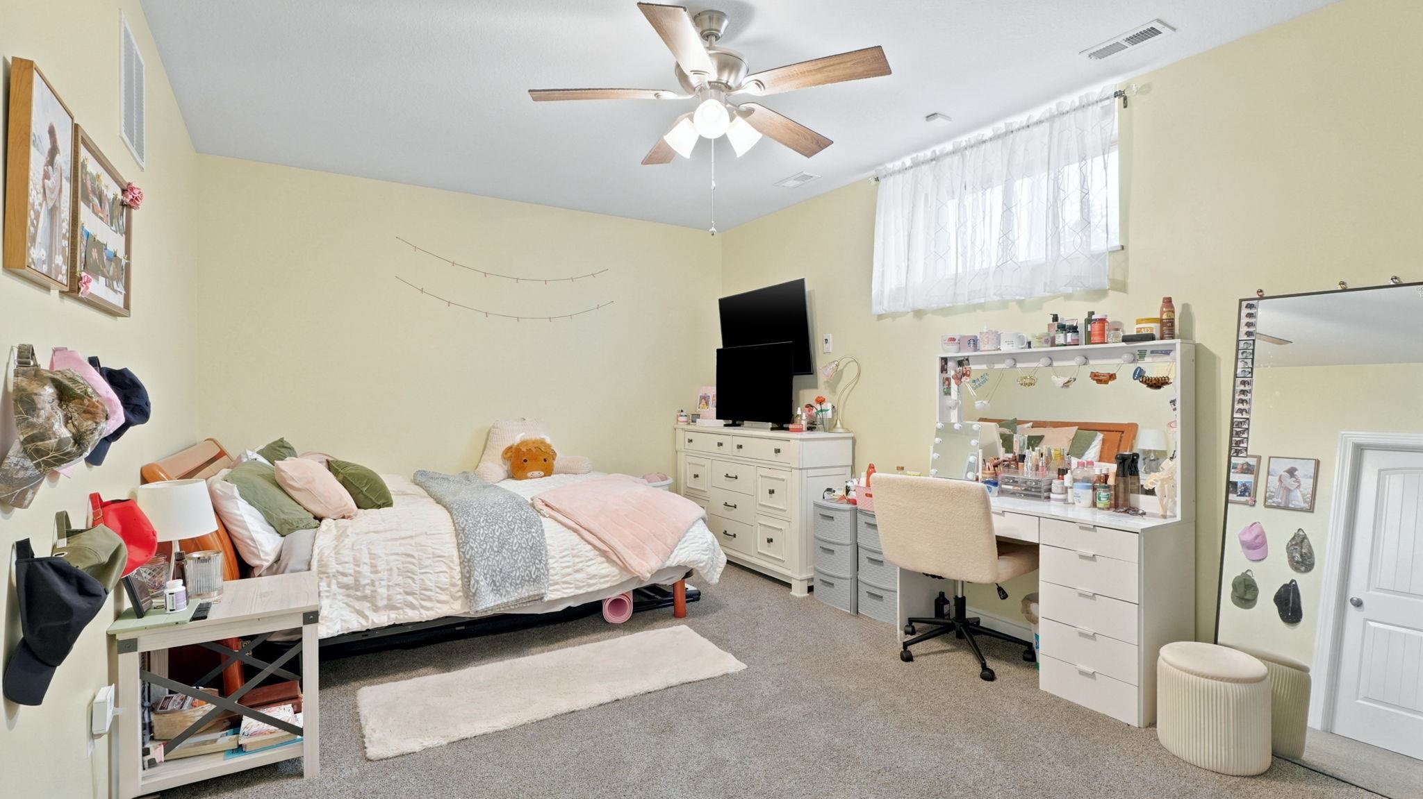 Carpeted room with a ceiling fan, light yellow wall paint, and a white window with curtain